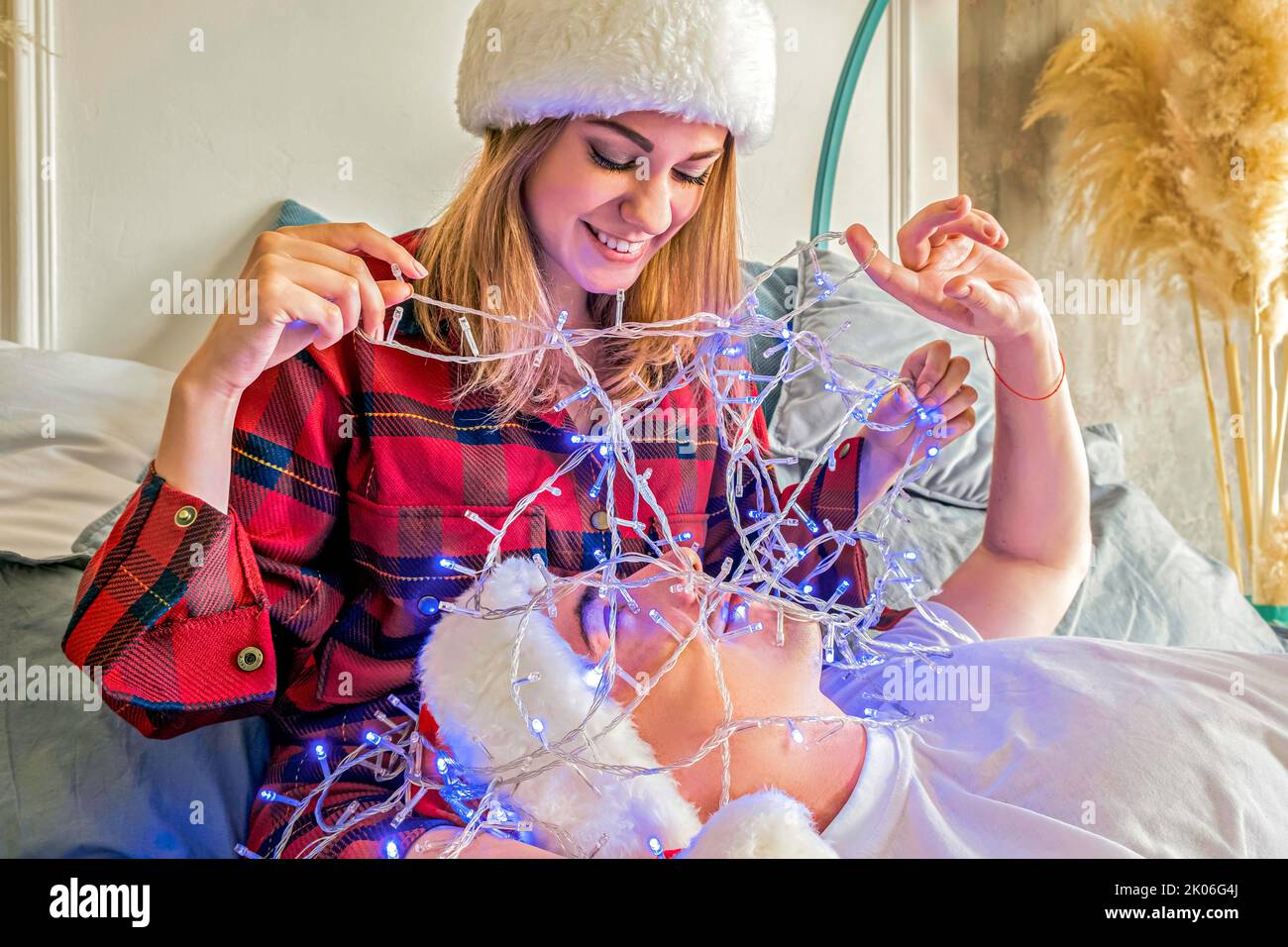 Natale. La giovane coppia celebra il Natale a casa sdraiata su un letto che indossa cappelli santa. Felice uomo e donna sorridono guardarsi l'un l'altro. L'uomo si trova su Foto Stock