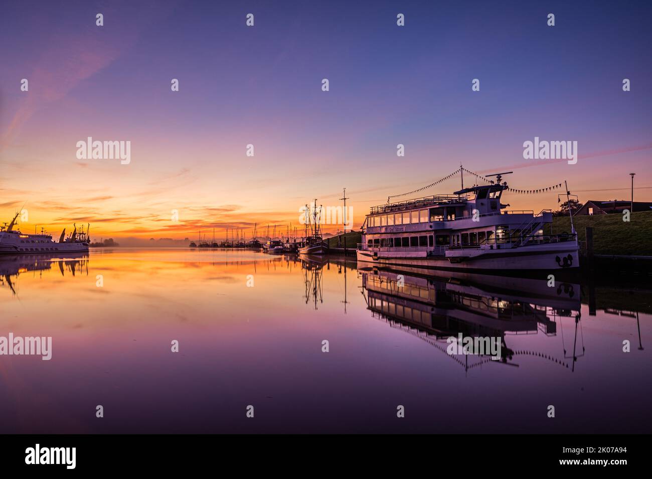 Poco di fronte all'alba nel porto di Greetsiel con le navi ancorate e la riflessione in acqua, Greetsiel, bassa Sassonia, Germania Foto Stock