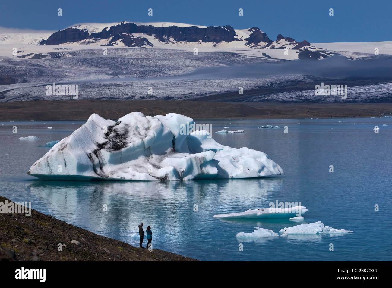 Due persone di fronte a un iceberg presso la laguna del ghiacciaio Joekulsarlon, il Parco Nazionale Vatnajoekull, Hornarfjoerdur, Islanda Foto Stock