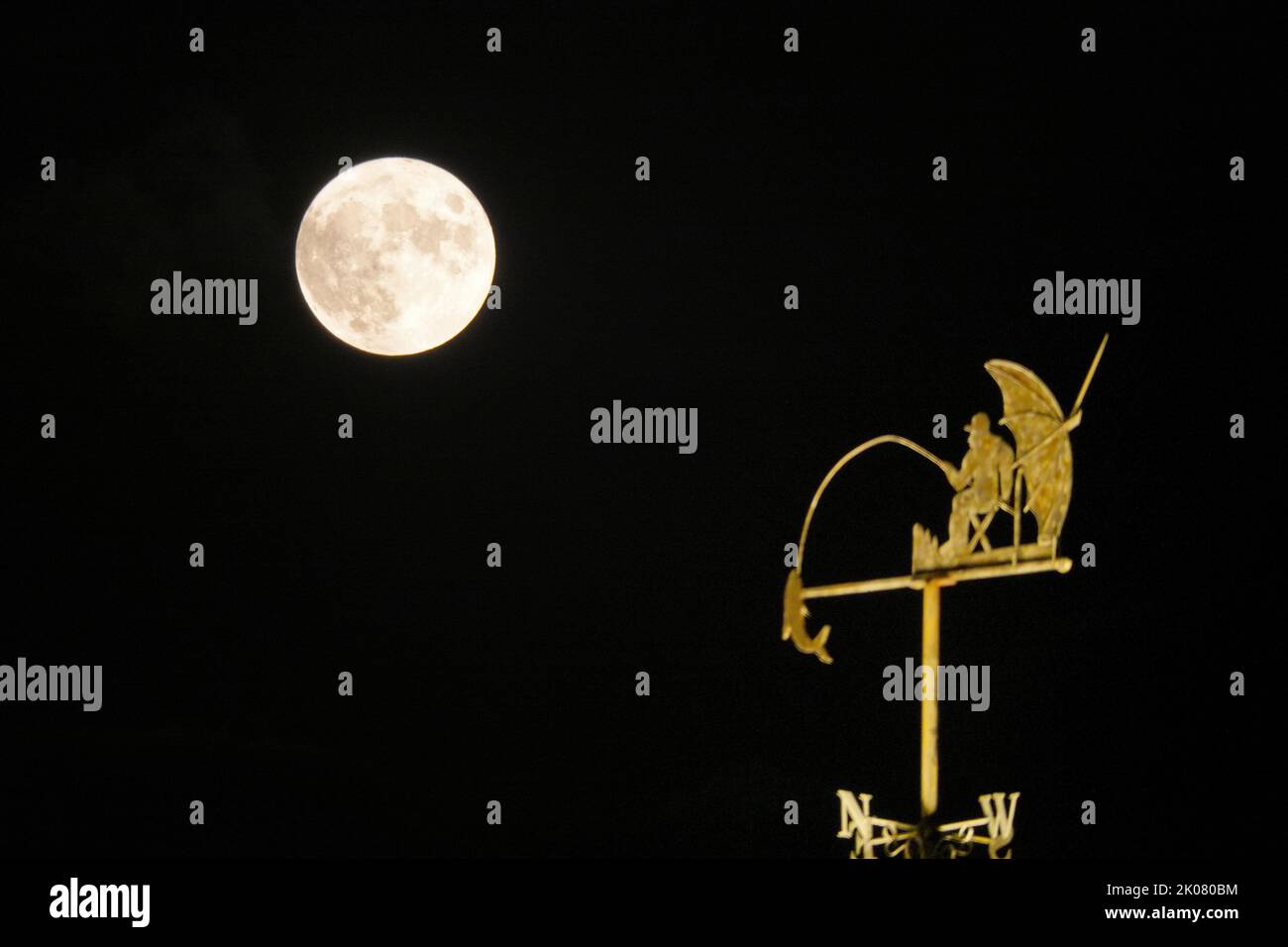 YANTAI, CINA - 10 SETTEMBRE 2022 - la luna piena di metà autunno passa sopra un weathervane sulla cima di un edificio a Yantai, provincia di Shandong, Cina, sulla S Foto Stock