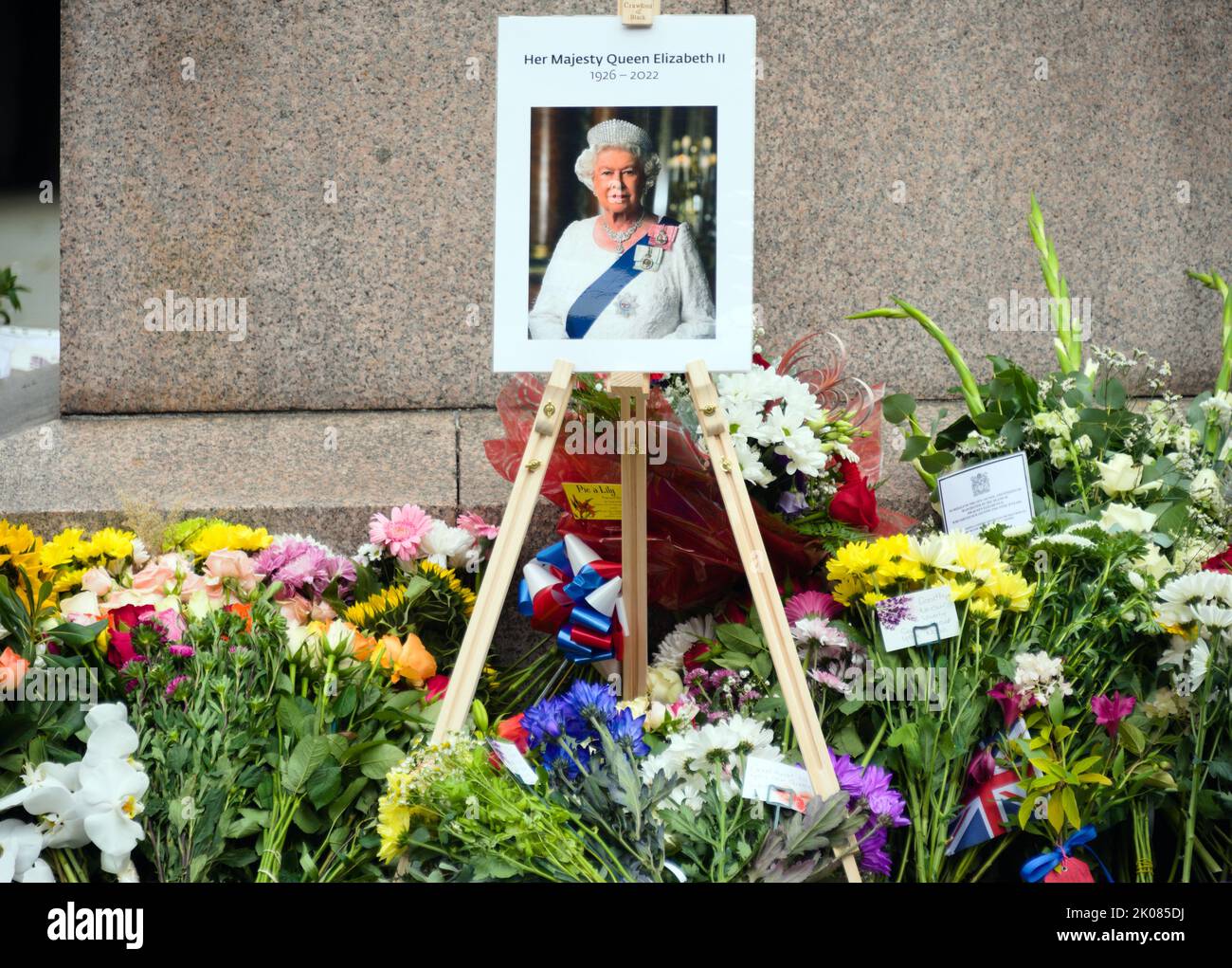 Manchester, Regno Unito, 10th settembre 2022. Una foto di sua Maestà, la Regina Elisabetta II, con i fiori lasciati in Piazza Sant'Anna, Manchester, Regno Unito, come omaggio a sua Maestà, la Regina. La Regina morì, all'età di 96 anni, il 8th settembre 2022. Il Manchester City Council ha dichiarato sul suo sito web che la città di Manchester osserverà il periodo ufficiale di lutto di 10 giorni e che: “I residenti potrebbero voler porre dei fiori per segnare la morte di sua Maestà. Potrete deporre fiori in Piazza Sant'Ann'. Credit: Terry Waller/Alamy Live News Foto Stock