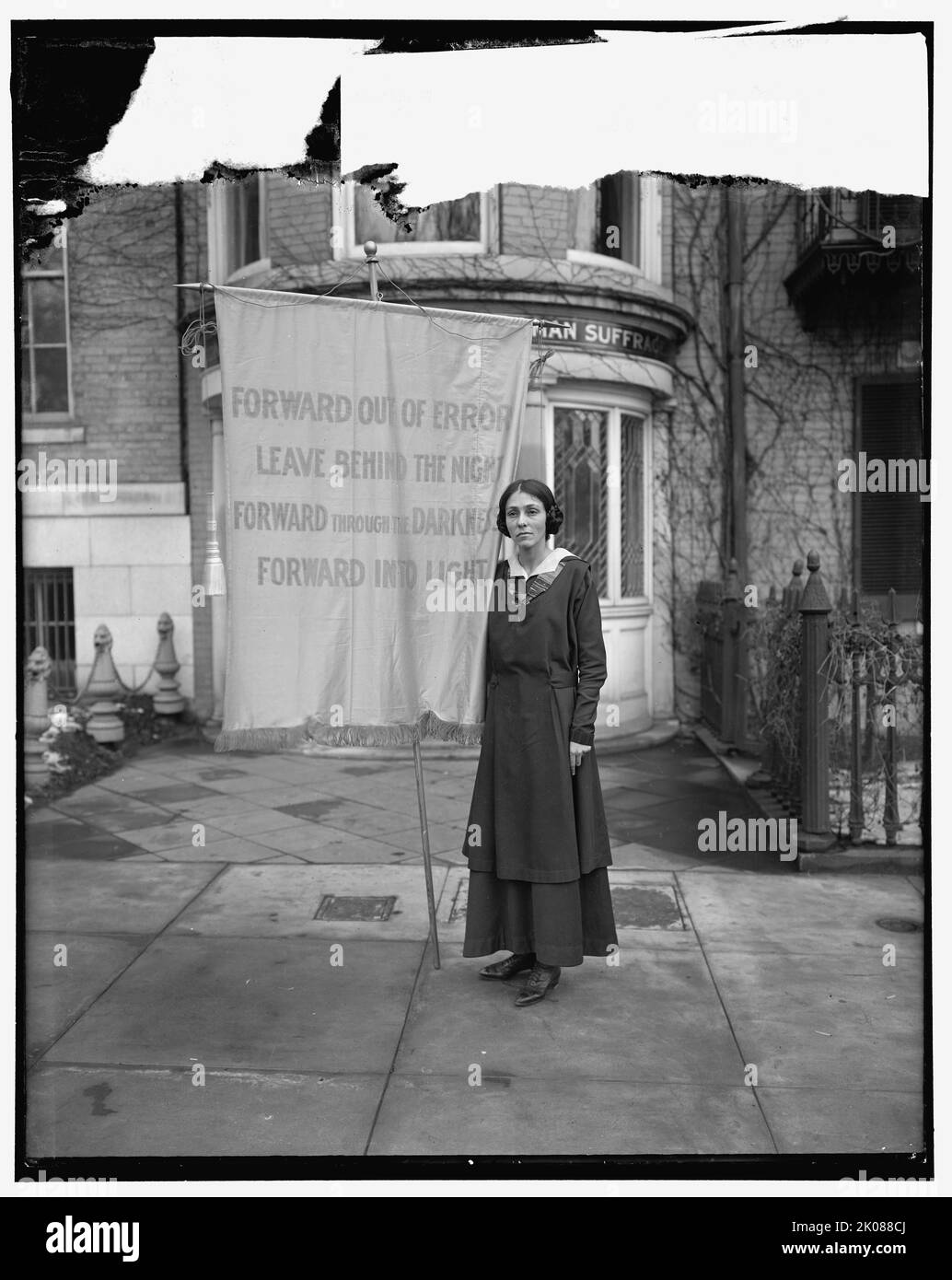 Unione Congressuale del suffragio femminile, tra il 1910 e il 1920. Donna con bandiera fuori Cameron House a Washington, DC, gli uffici del Congressional Union for Woman Suffrage. Il banner recita: 'Avanti per errori, lasciare dietro la notte; avanti attraverso l'oscurità, avanti nella luce'. Foto Stock