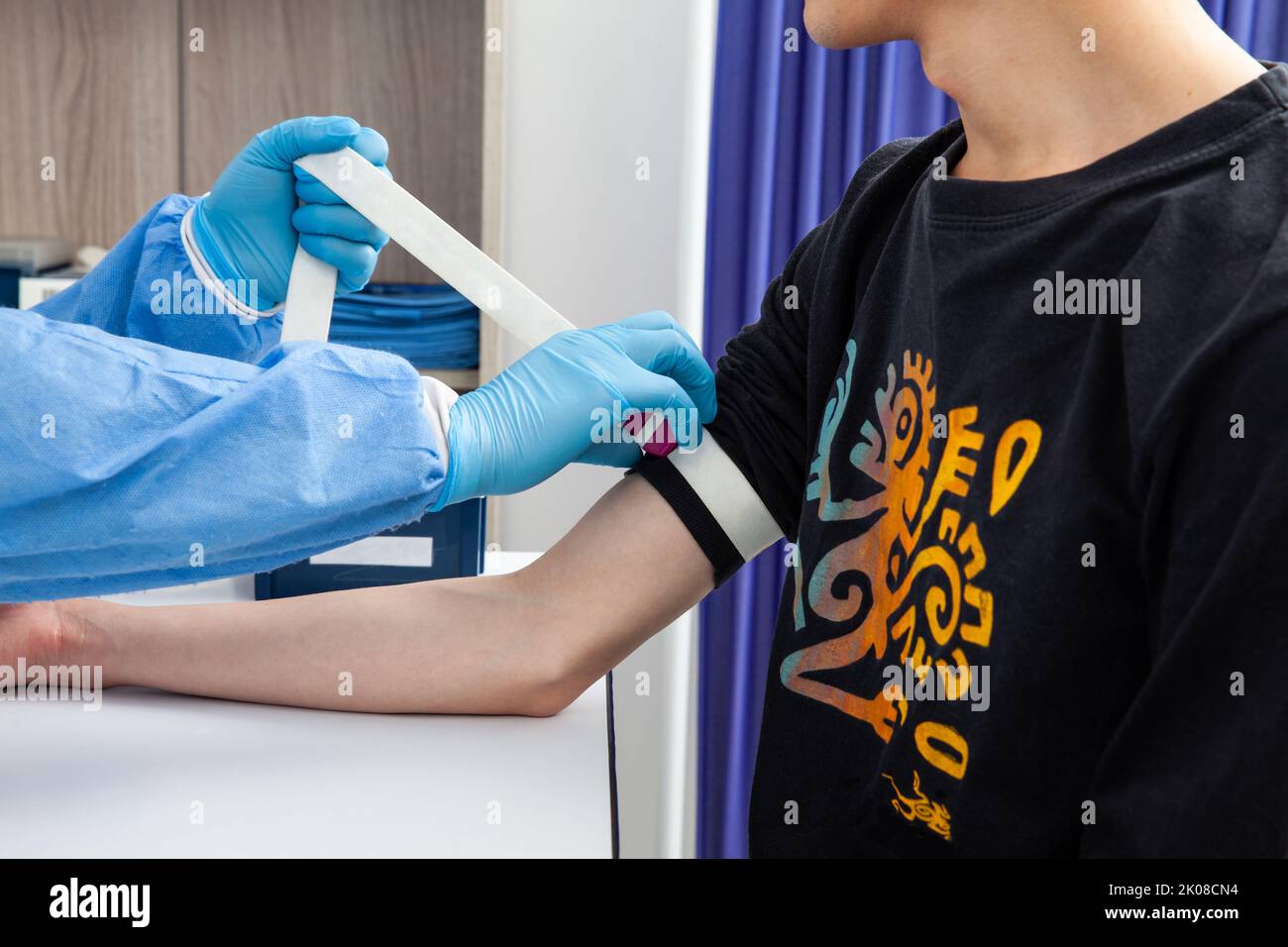 Infermiera che stringe la fascia elastica sul braccio di un paziente maschio per prelevare un campione di sangue da una clinica Foto Stock