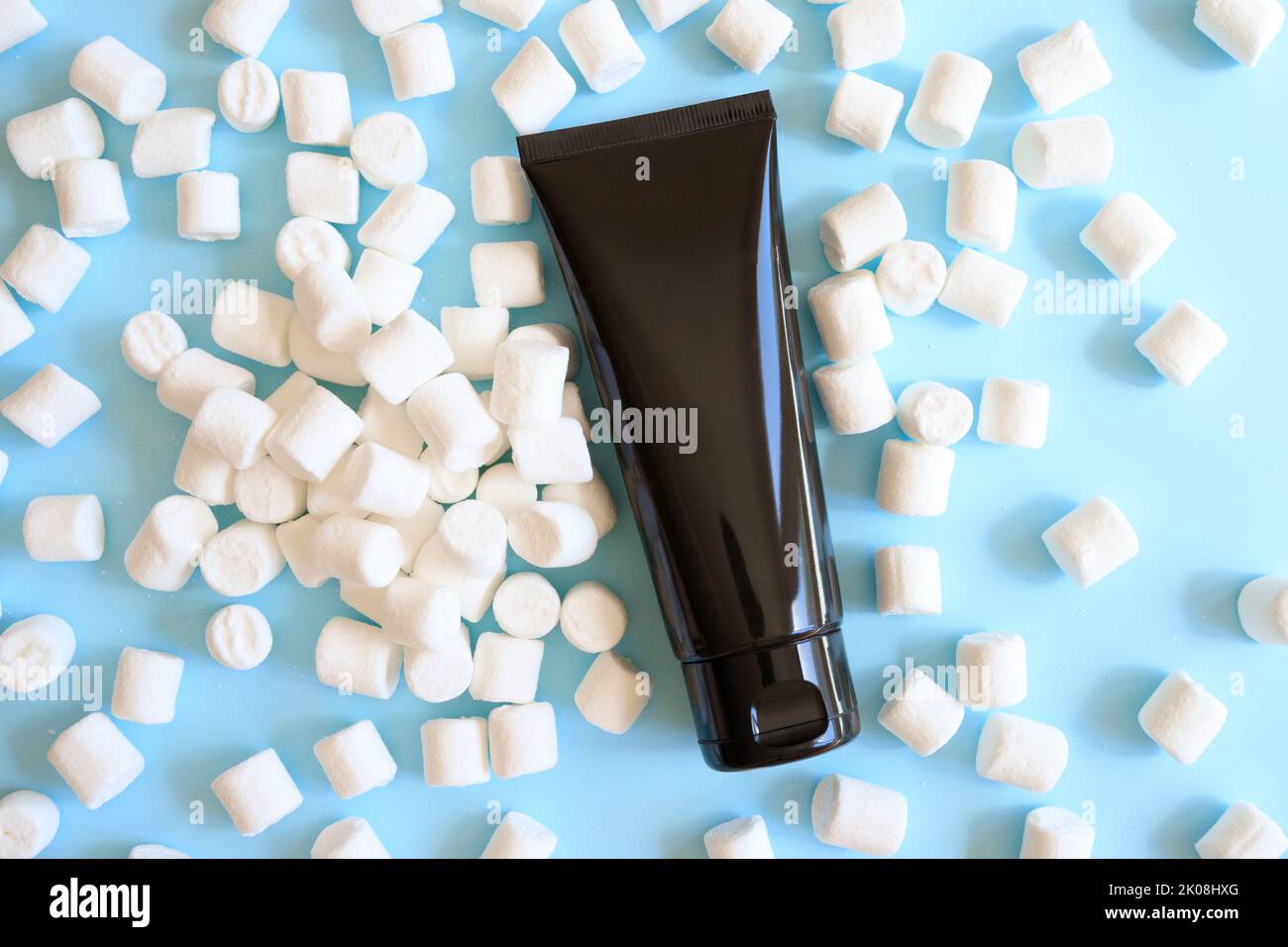 Mockup nero spremere bottiglia tubo cosmetico e bianco mini marshmallows mólto su sfondo blu. Crema, gel lubrificante, idratante, cura della pelle, crema solare Foto Stock