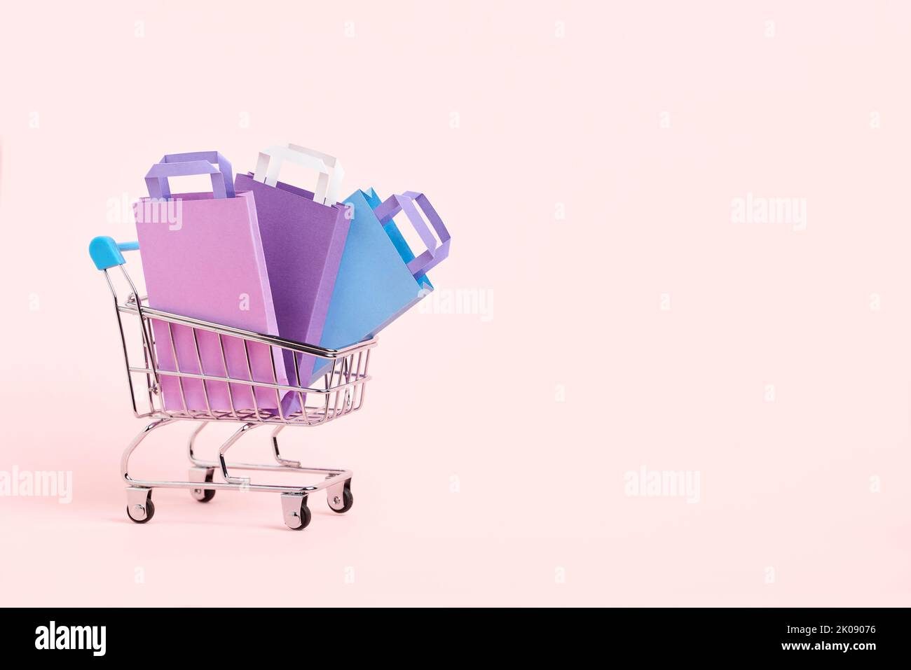 Carrello con sacchetti di carta viola, lilla e blu su sfondo rosa pastello. Design minimalista con spazio copia. Concetti: Offerte di mercato, stagionali Foto Stock