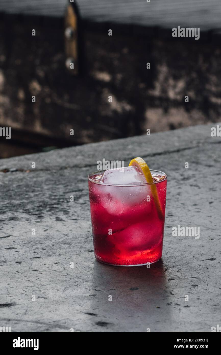 drink da cocktail con arbusto di mirtillo magenta rosa brillante con rotella al limone e ghiaccio su cemento Foto Stock
