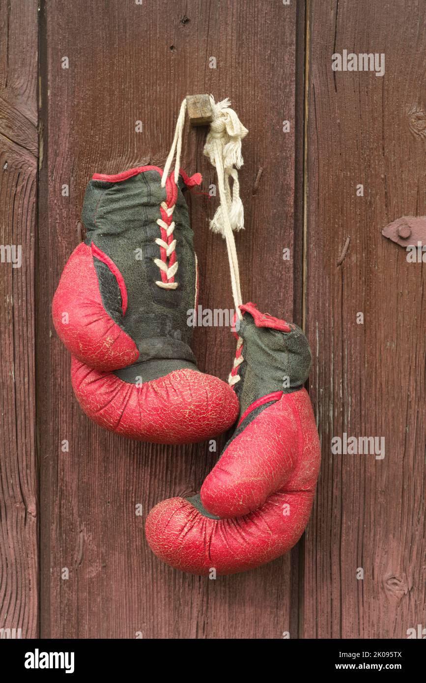 I vecchi guanti da boxe rossi in pelle appendono sullo sfondo del legno in marrone Foto Stock
