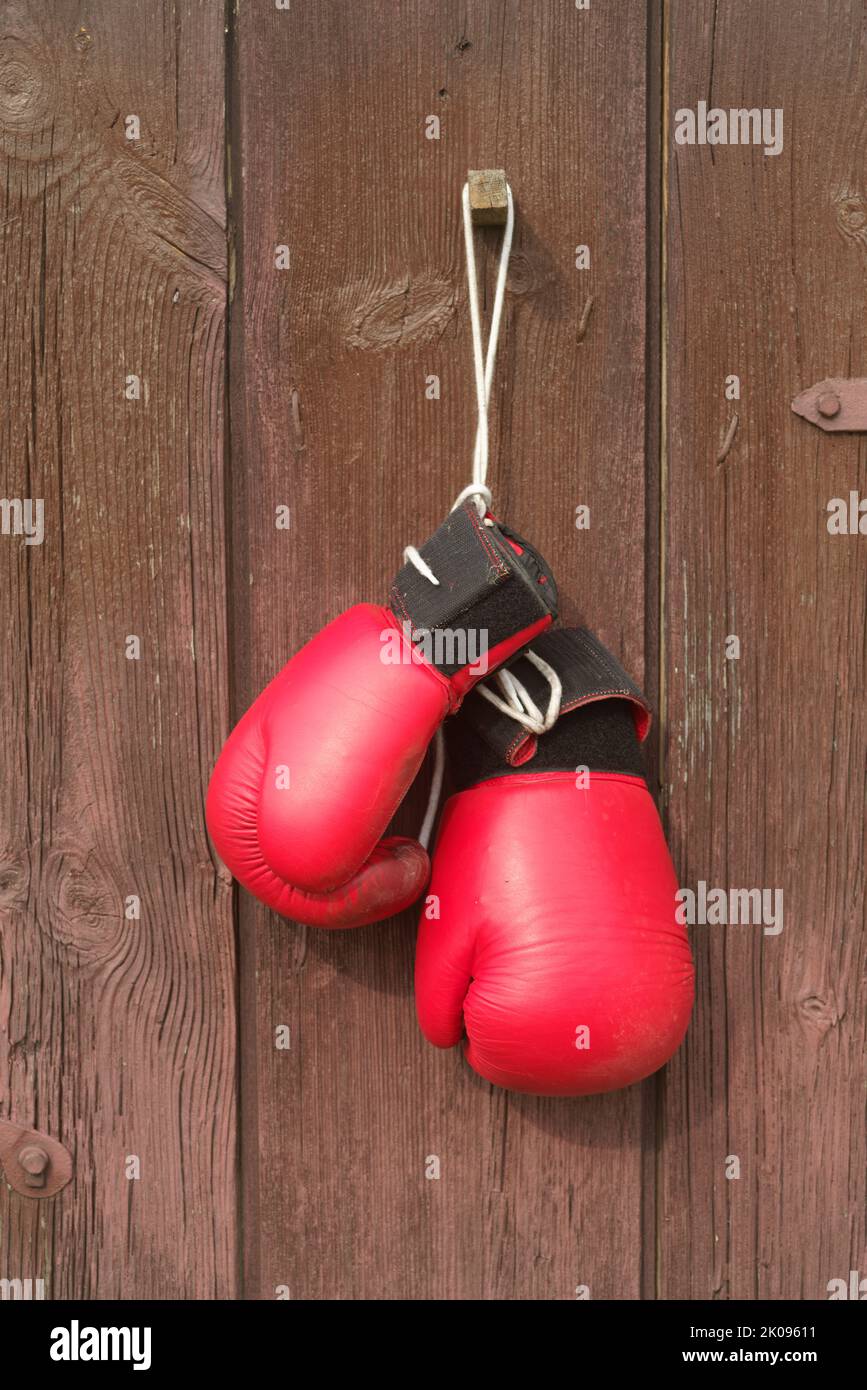 I vecchi guanti da boxe rossi in pelle appendono sullo sfondo del legno in marrone Foto Stock