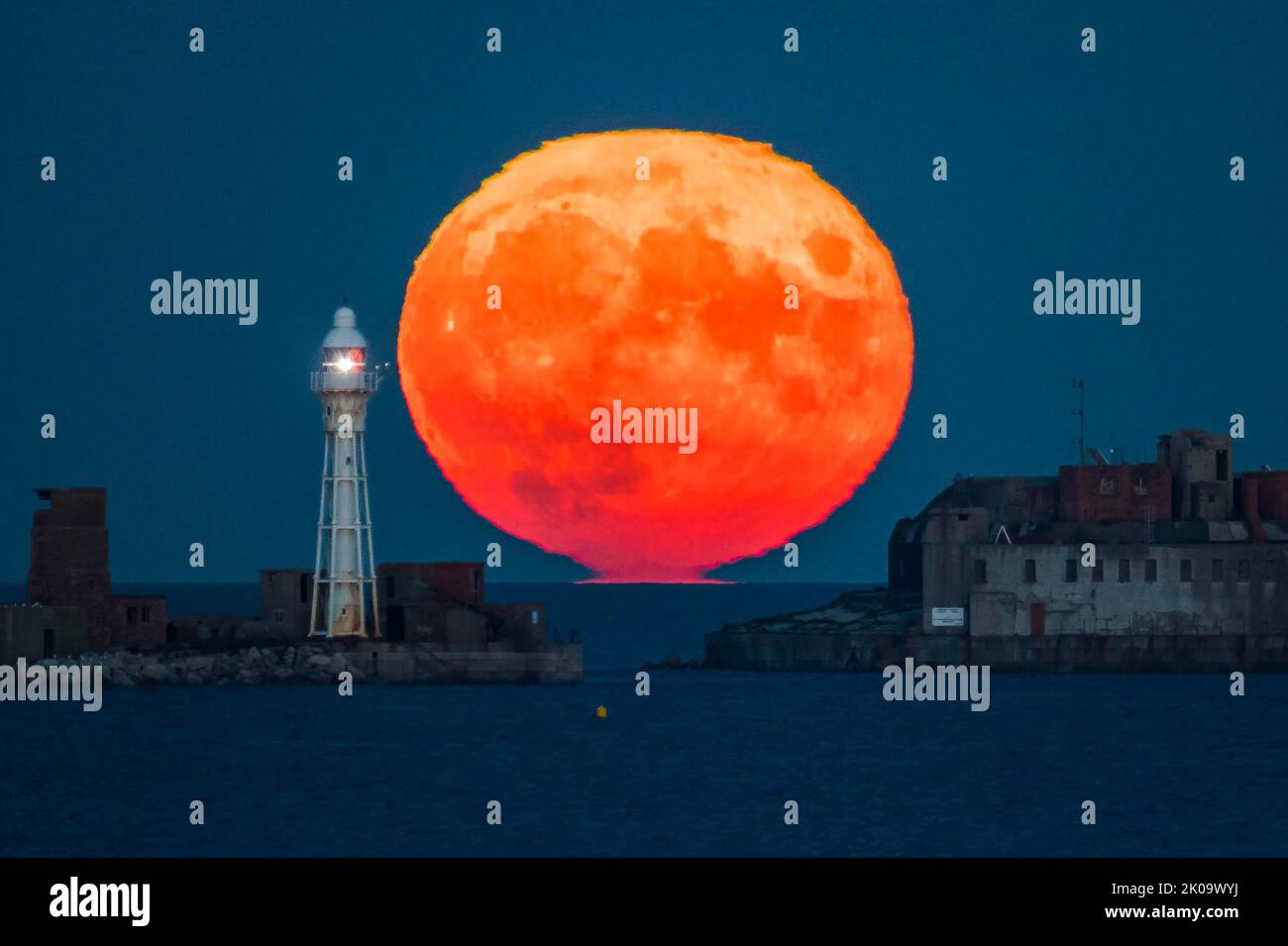 Weymouth, Dorset, Regno Unito. 10th settembre 2022. Meteo nel Regno Unito. Il Full Harvest Moon sorge tra il faro e lo storico Portland Breakwater Fort del 19th° secolo sul frangiflutti esterno del Porto di Portland nel Dorset. Il forte ora derelitto anche conosciuto come Chequered Fort è stato costruito tra il 1868 e il 1878 ed è classificato di II grado. Picture Credit: Graham Hunt/Alamy Live News Foto Stock