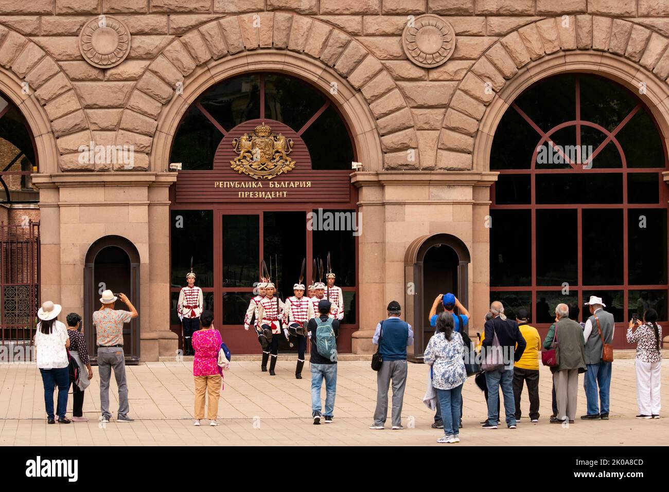 Gruppo di turisti che partecipano alla cerimonia del cambio delle guardie al di fuori dell'edificio della Presidenza bulgara, Sofia, Bulgaria, Europa orientale, Balcani, UE Foto Stock