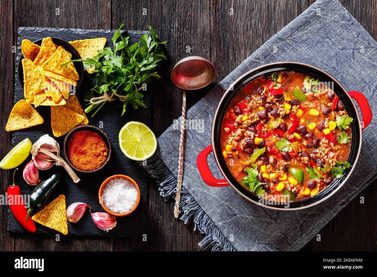 zuppa di taco di macinato di manzo, pomodori, peperoncino verde tritato, cipolle, mais, fagiolini rossi e taco condimento in pentola rossa con ingredienti su tavola di pietra, alto Foto Stock