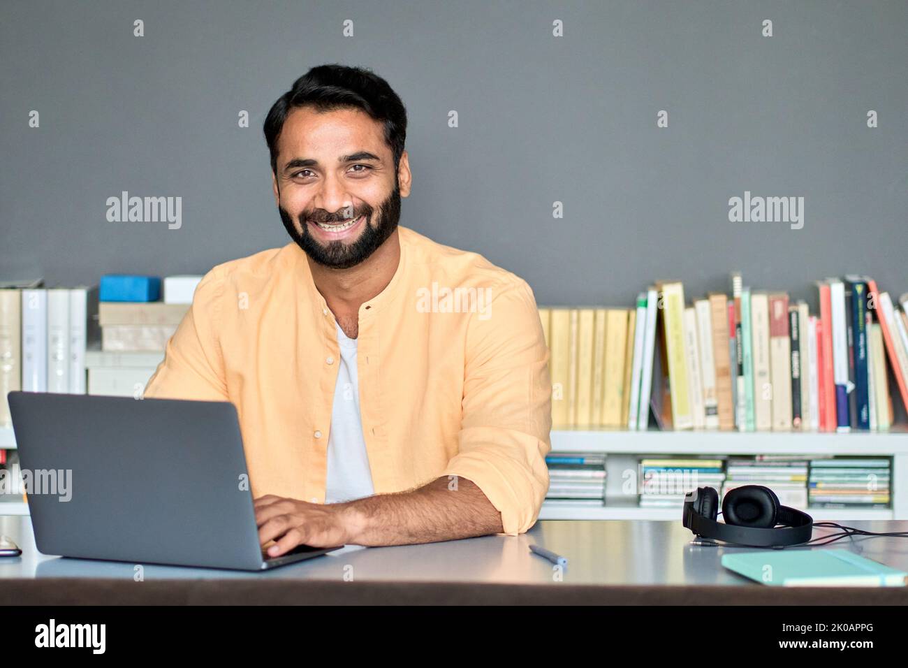 Uomo d'affari indiano felice che lavora su un computer portatile in ufficio seduto alla scrivania, ritratto. Foto Stock