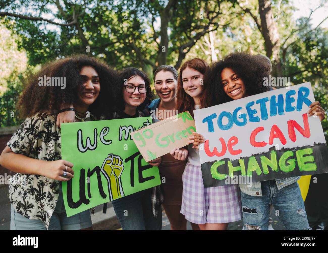 Attivisti adolescenti multiculturali sorridono alla macchina fotografica mentre tengono poster e cartelloni durante una protesta pacifica. Gruppo di dimostratori di generazione z Foto Stock