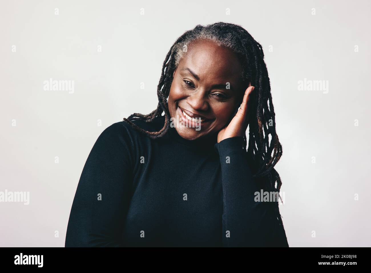 Donna matura sicura di sé sorridente alla fotocamera mentre tocca i suoi spaventosi lucchetti. Allegra donna di mezza età che abbraccia con orgoglio i suoi capelli naturali. HAP Foto Stock