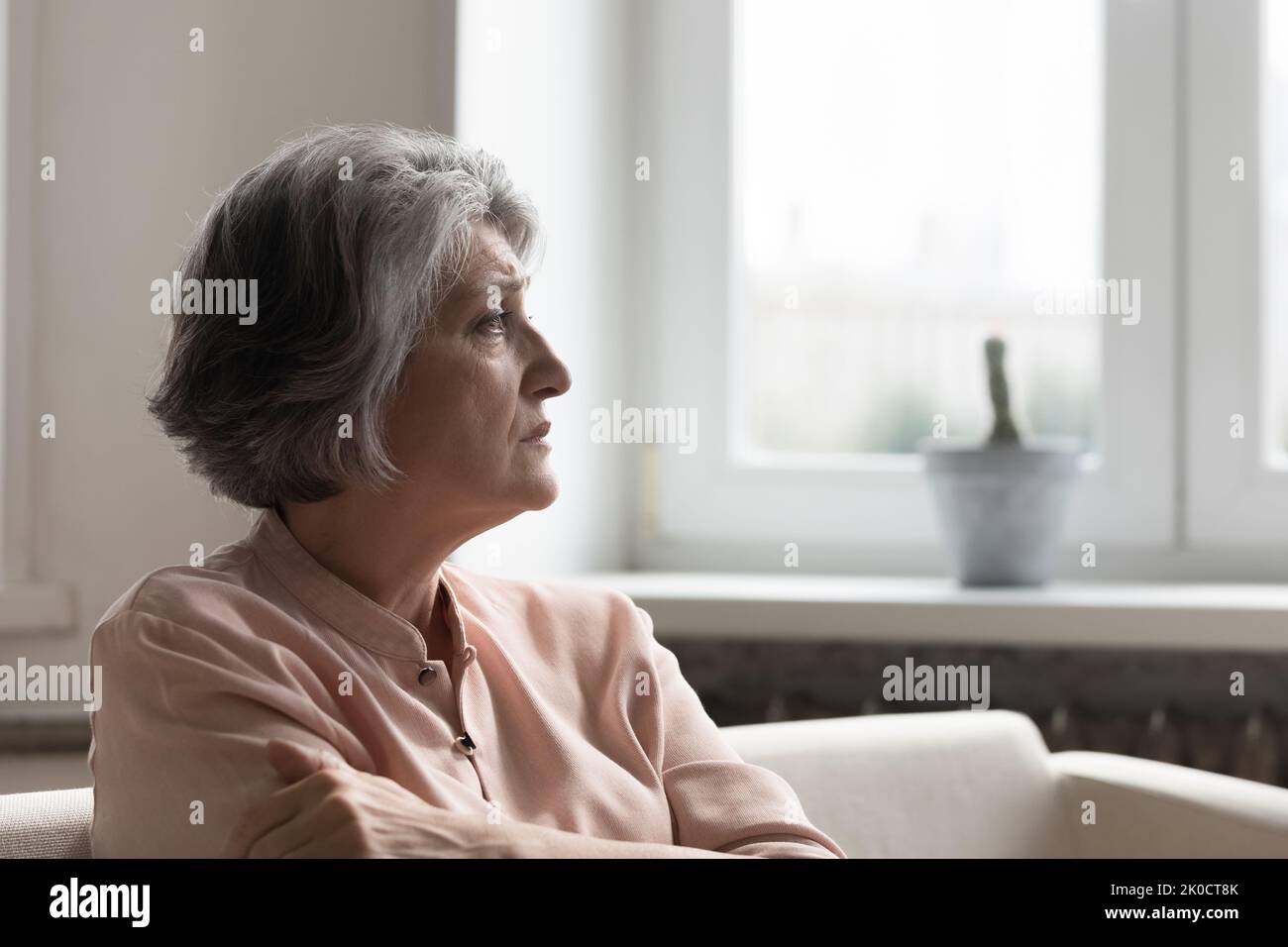 Preoccupata donna anziana ansiosa di 60s anni che guarda via, seduto sul divano Foto Stock