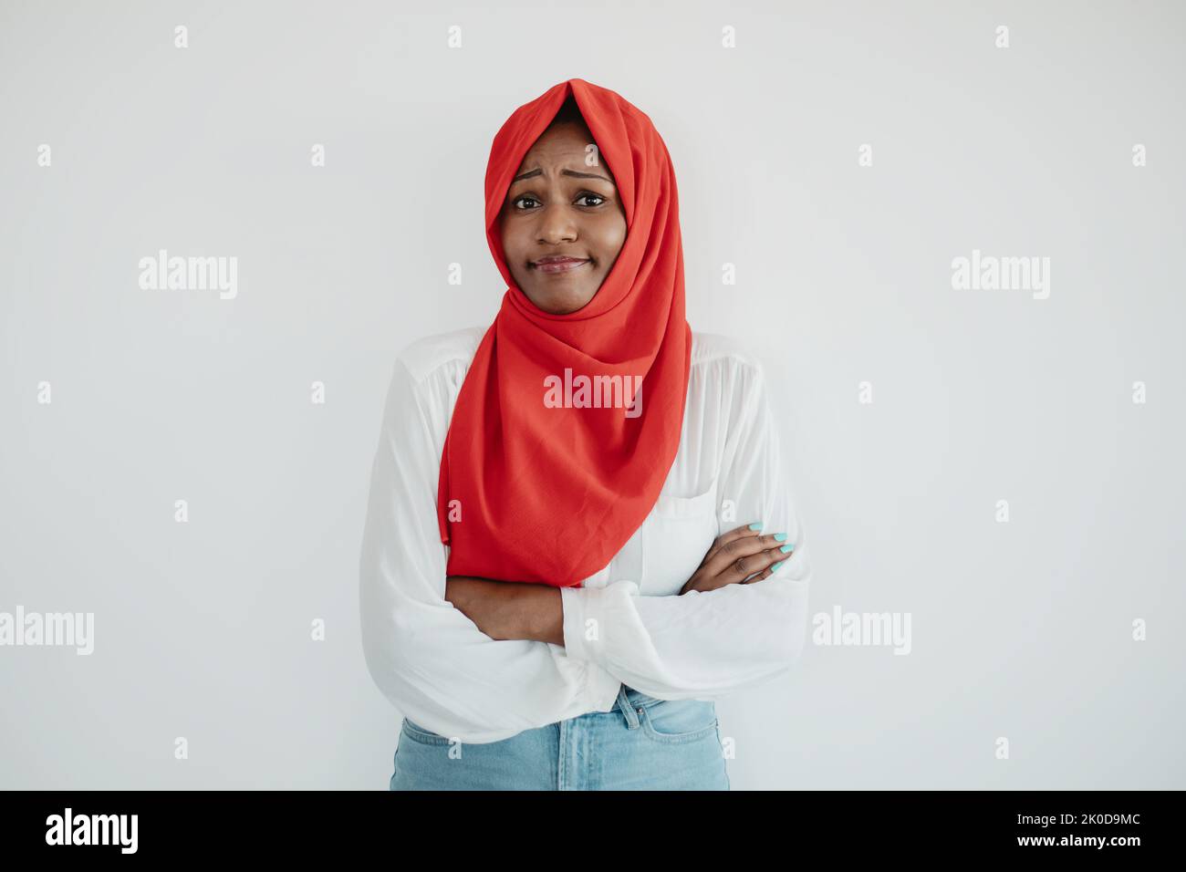 Concetto di emozioni della gente. Offesa triste donna musulmana nera che posava con le braccia ripiegate sopra la parete di uno studio luminoso Foto Stock