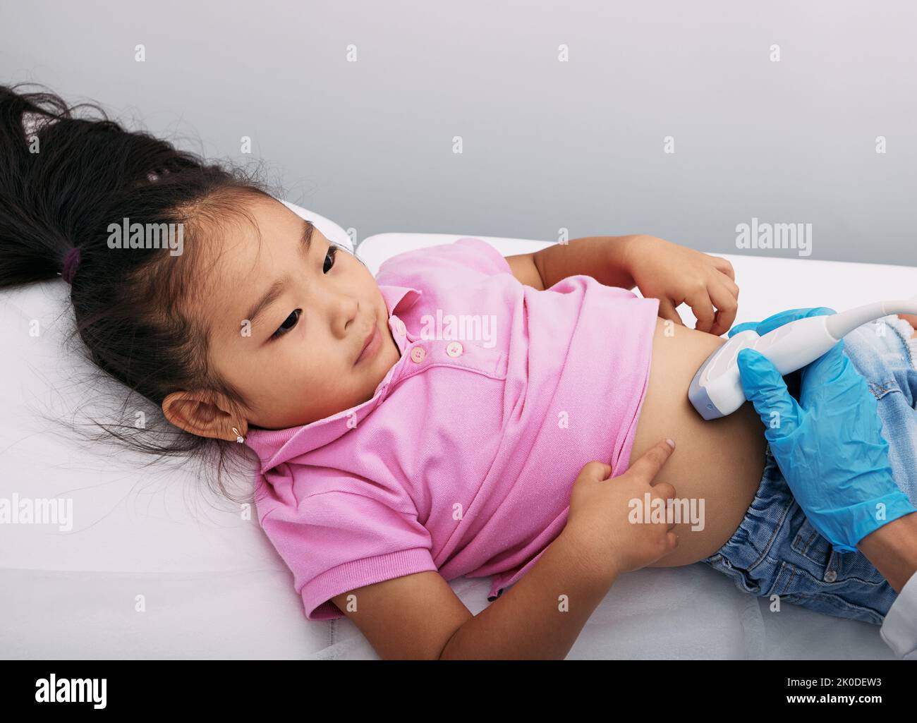 La bambina asiatica paziente riceve la diagnostica del ventre con la macchina a ultrasuoni, primo piano. medico con trasduttore a ultrasuoni che esegue la scansione addominale e inter Foto Stock