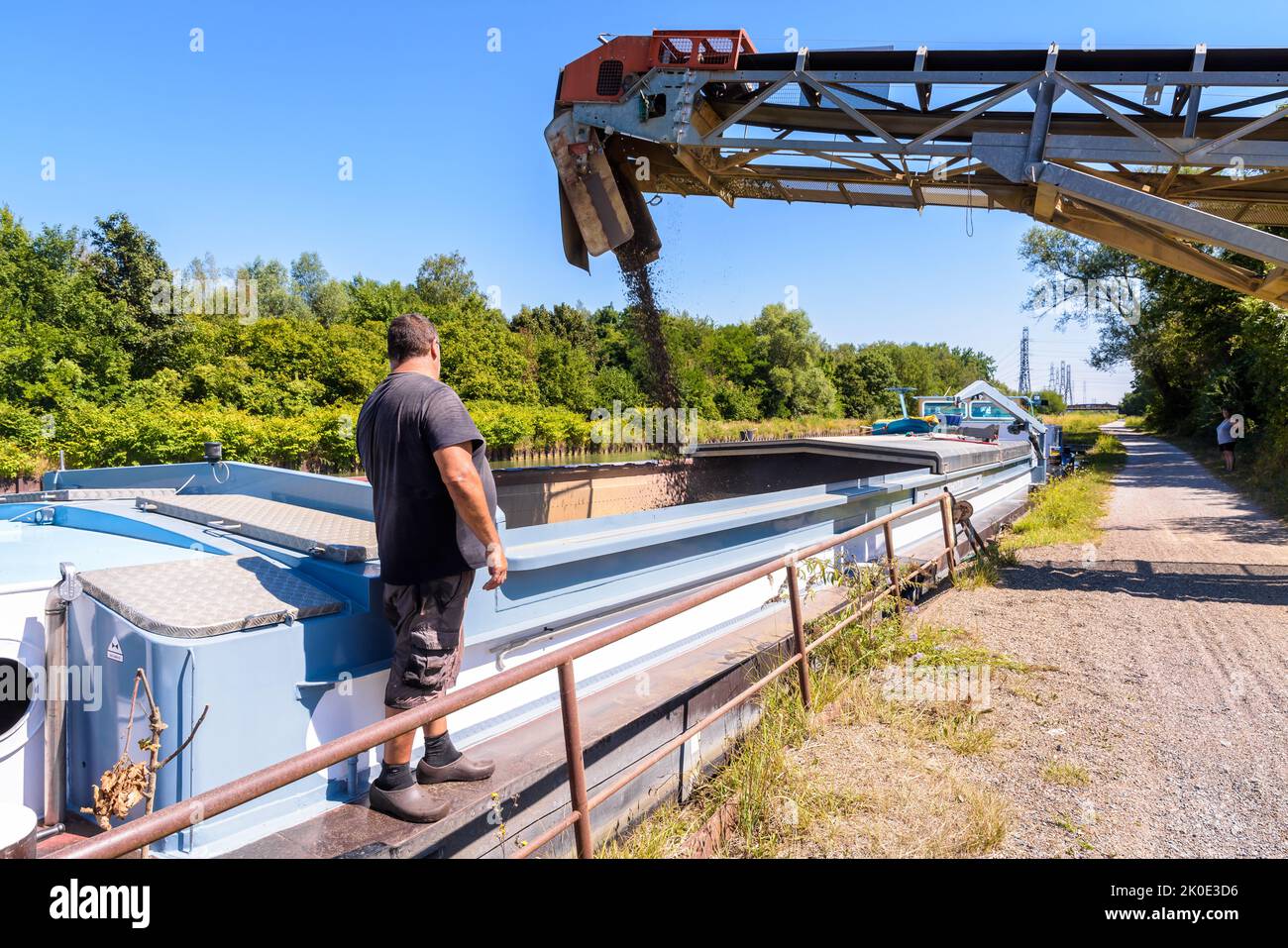 Un bargeman sta guardando il carico con la ghiaia della sua chiatta motorizzata ormeggiata su un canale in una cava di sabbia in una giornata di sole estate. Foto Stock