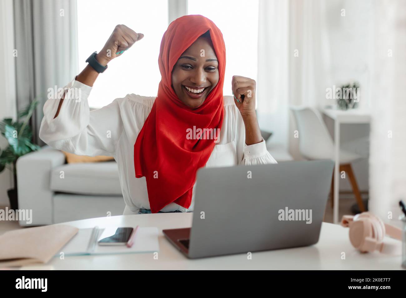 Ottime notizie. Entusiasta musulmana afro-americana festeggia il successo, guardando lo schermo del notebook, alzando pugni ed esclamando Foto Stock