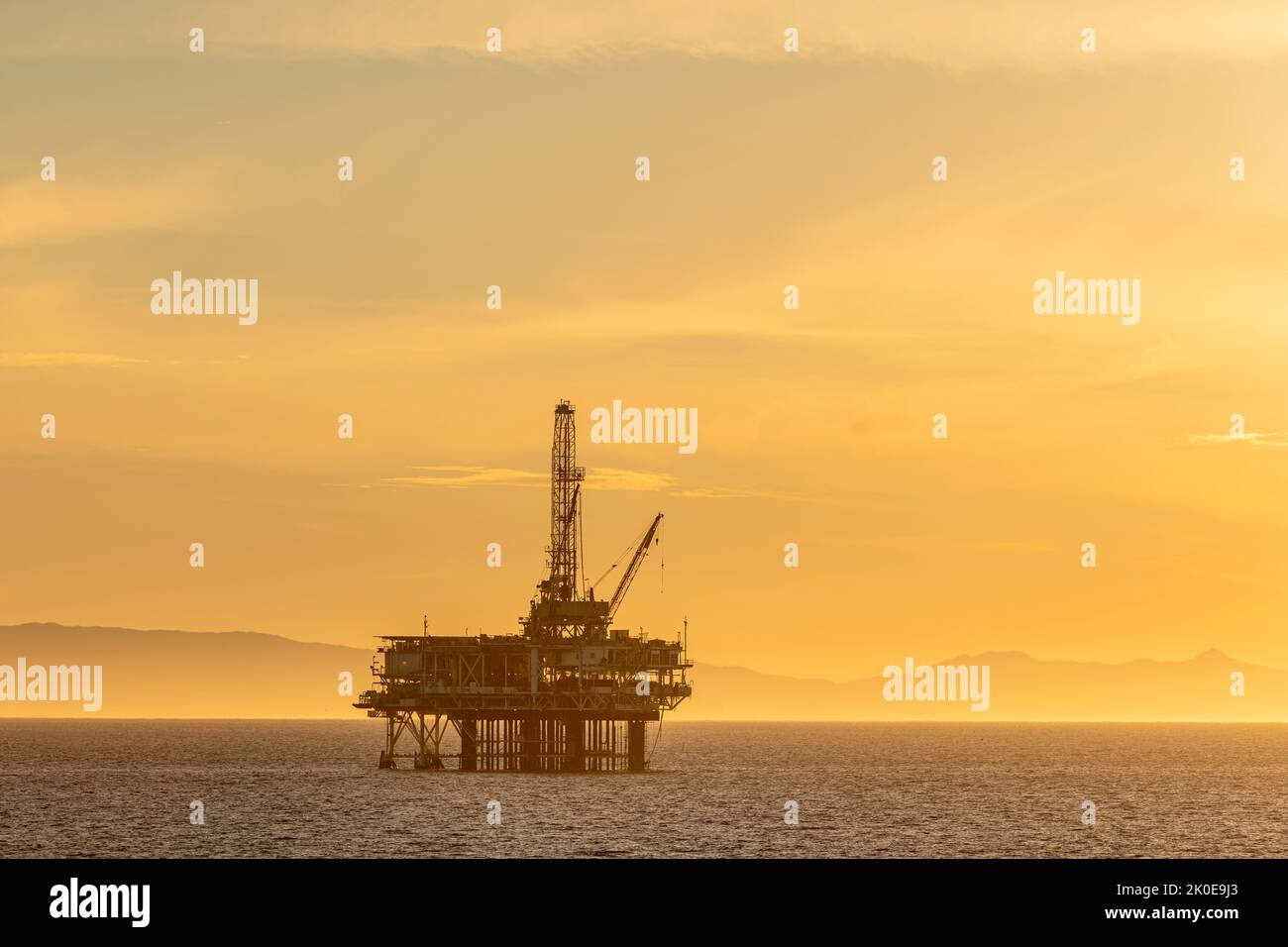 Immagine drammatica di una piattaforma petrolifera offshore al largo della costa della California contro un cielo giallo invernale al tramonto del sole. Foto Stock