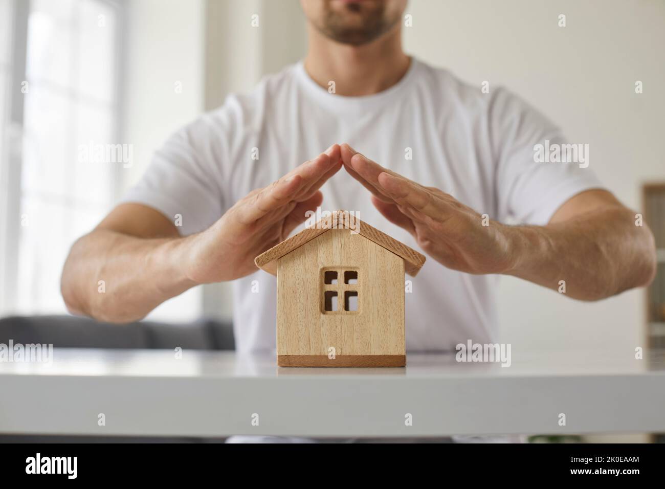 L'uomo fa la protezione del tetto sopra la piccola casa con le sue mani, simbolizzando la sicurezza e l'assicurazione. Foto Stock