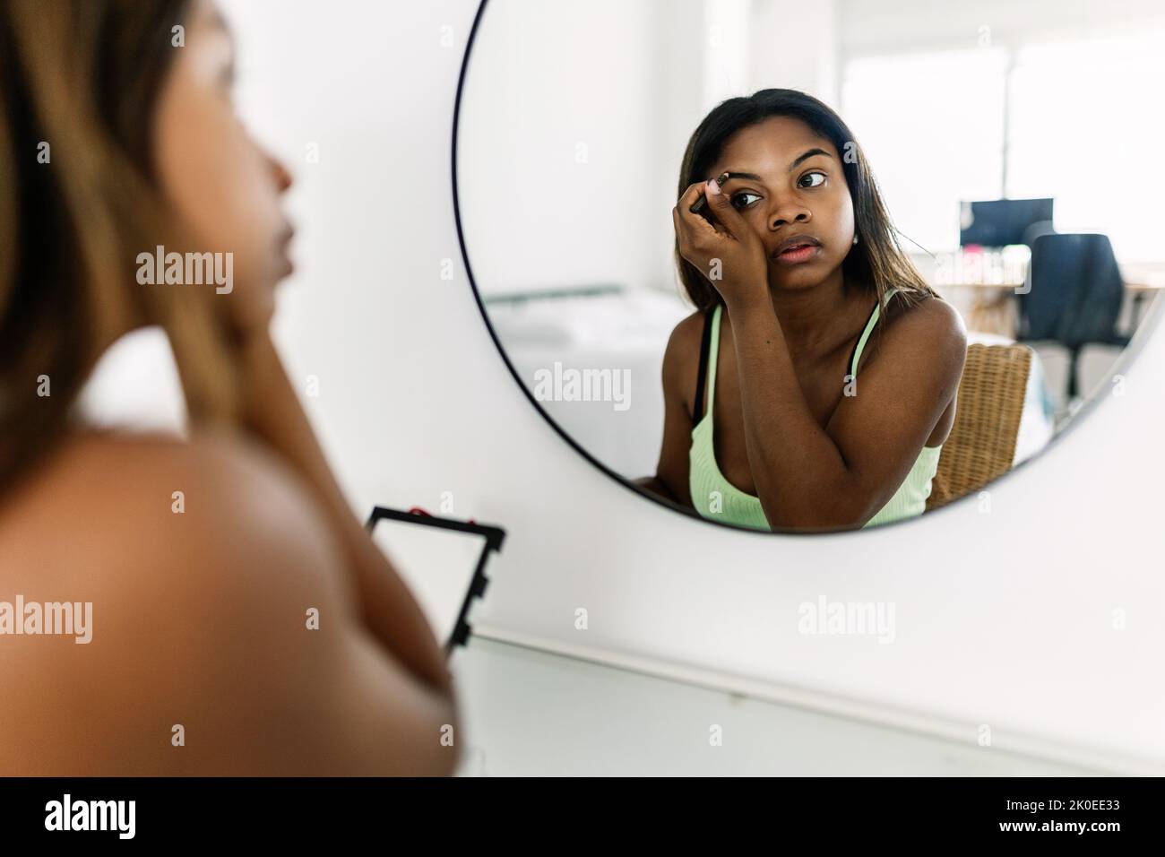 Giovane donna ispanica latina che applica il trucco di fronte allo specchio in camera da letto Foto Stock