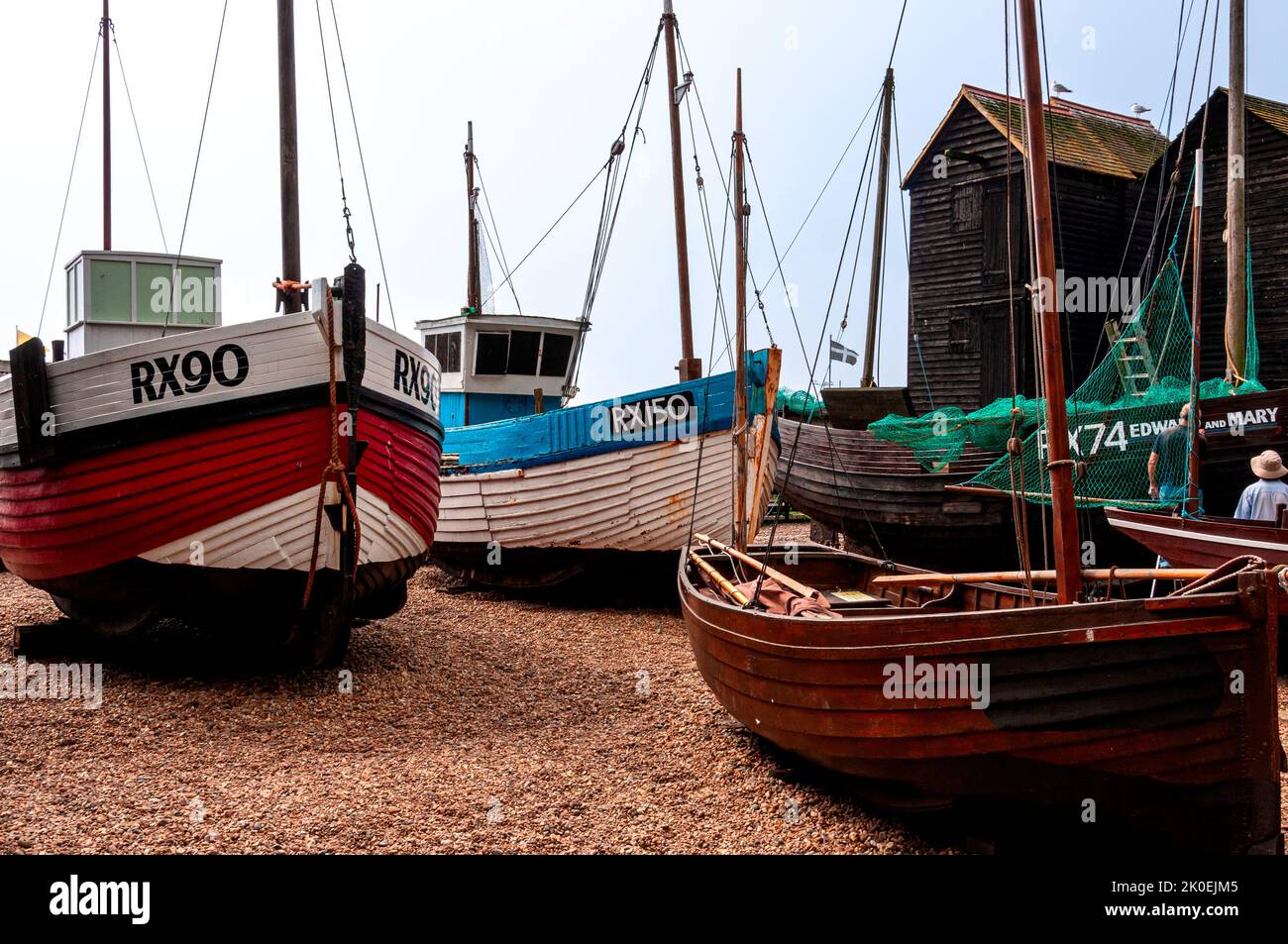 Una varietà di vecchie barche da pesca di proprietà dei pescatori, Museo esposto sulla spiaggia di ciottoli la Stade di fronte a due negozi di alta rete, Hastings Foto Stock