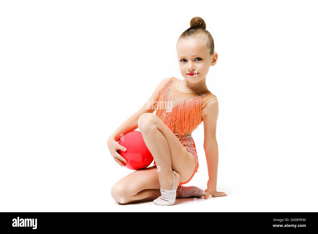 Piccola ragazza ginnastica studio ritratto con palla di gomma, acrobazie artistiche e sport professionale per i bambini. La ragazza si siede su un ginocchio. Foto Stock