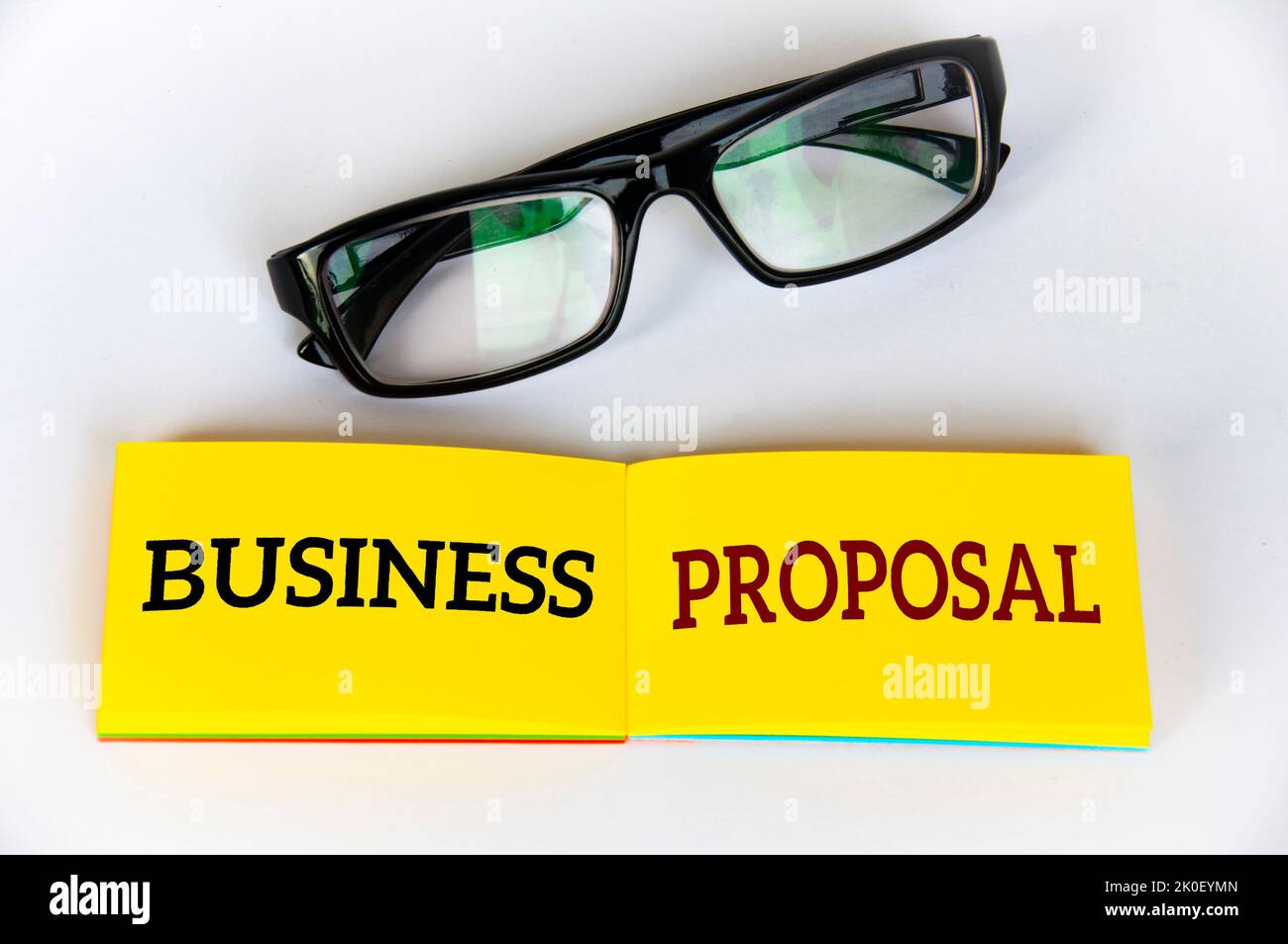 Vista dall'alto del testo della proposta commerciale su blocco note giallo con vetri su sfondo bianco. Concetto aziendale. Foto Stock