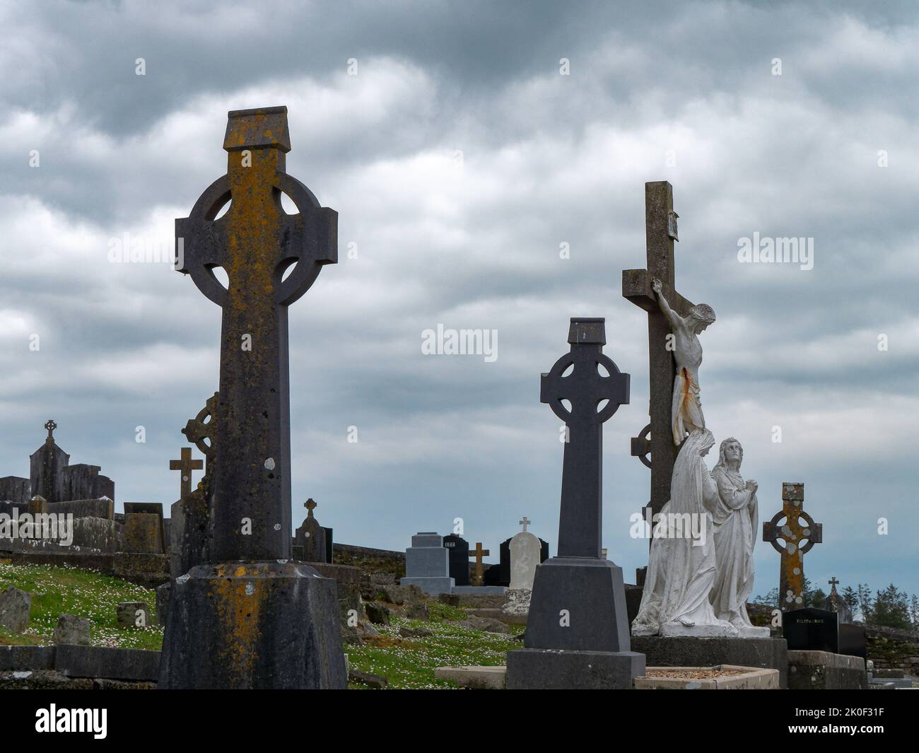 West Cork, Irlanda, 2 maggio 2022. Lapidi sotto forma di croci celtiche in un vecchio cimitero cattolico in una giornata nuvolosa, attraversare la statua sotto le nuvole bianche Foto Stock