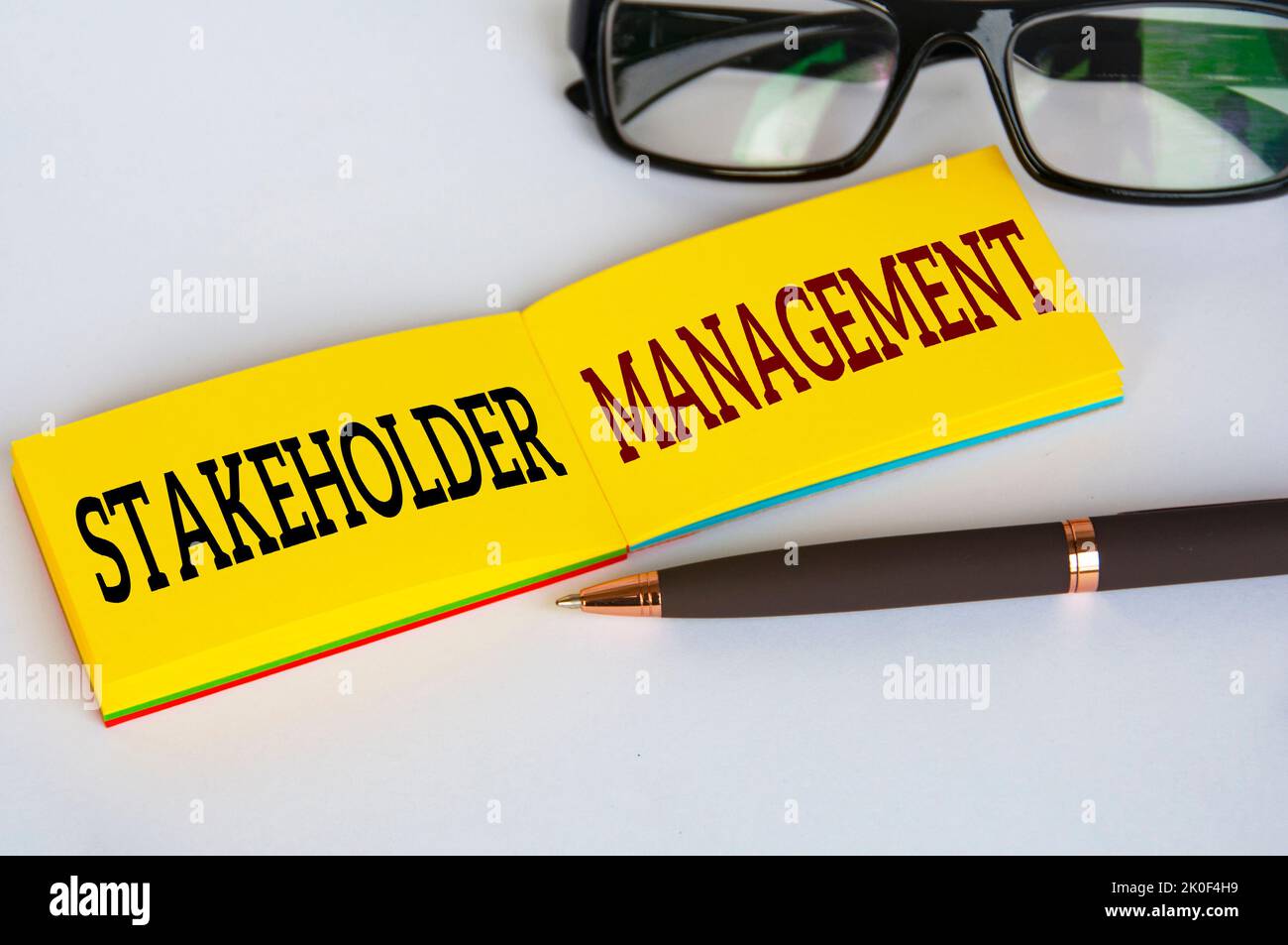 Testo di gestione degli stakeholder su blocco note giallo con occhiali e penna su sfondo bianco. Concetto di rapporto di affari. Foto Stock