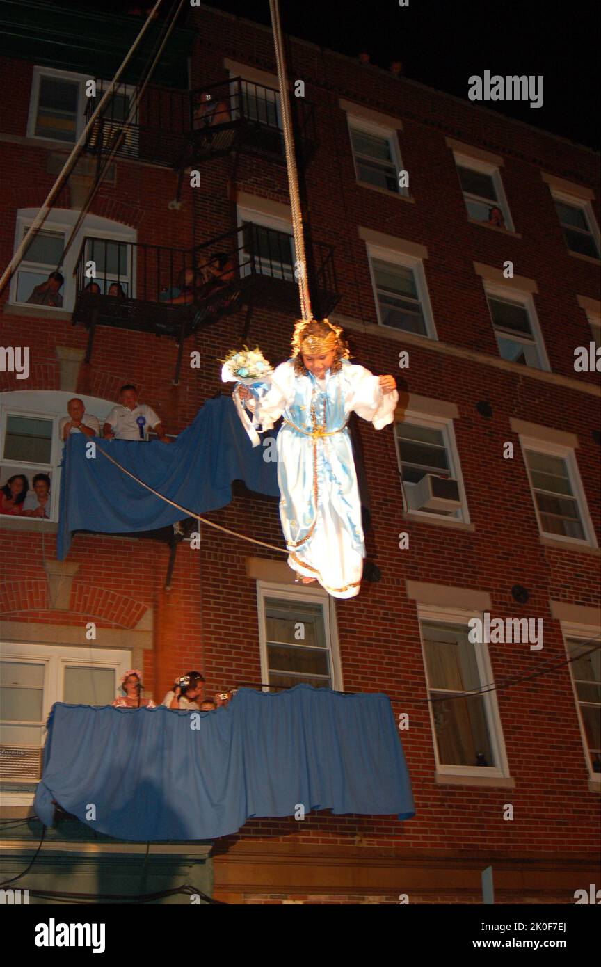 Una ragazza sospesa da un cavo galleggia a terra durante la celebrazione religiosa Flight of the Angela nella festa dei pescatori di Boston nel North End Foto Stock