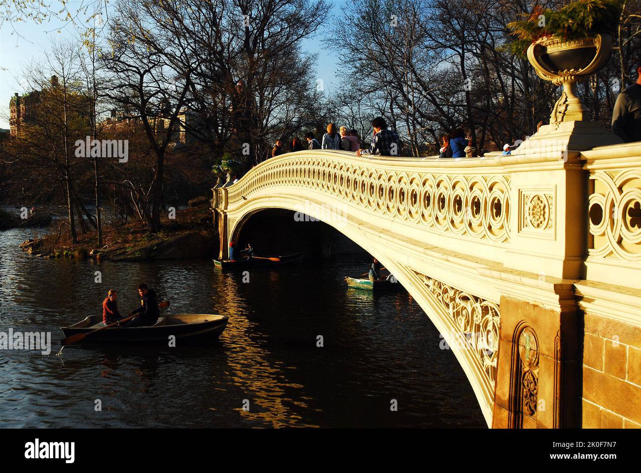 Due amici prendono una barca a remi sul lago in una giornata primaverile, passando sotto il Bow Bridge a Central Park, New York City Foto Stock