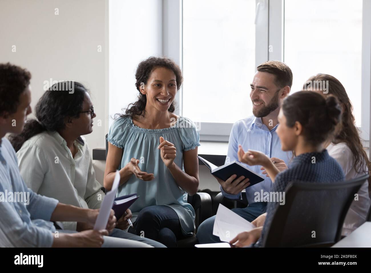 Felice diversi dipendenti seduti su sedie in cerchio, parlando Foto Stock