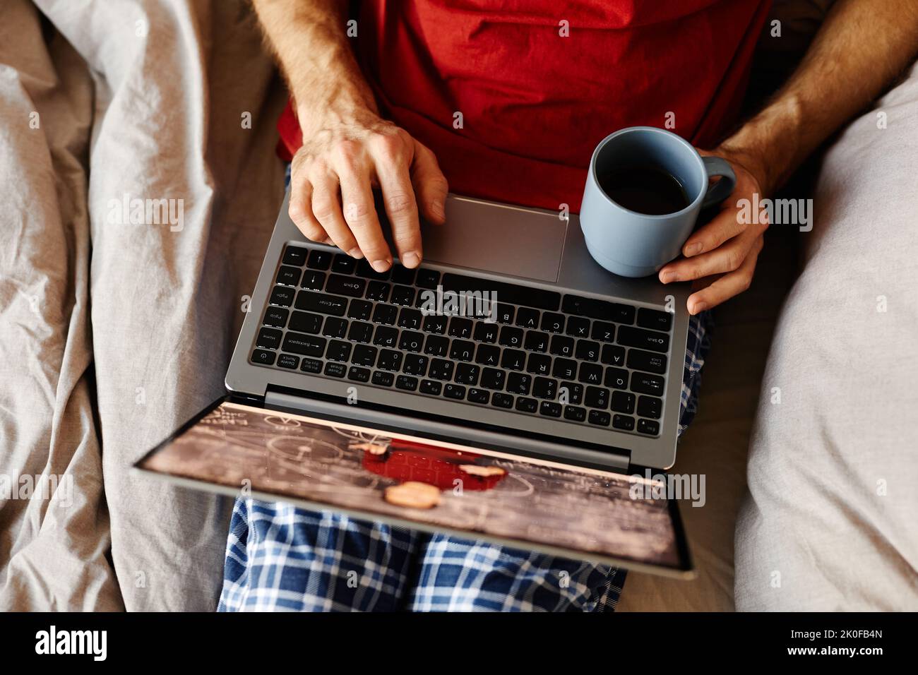 Vista ad angolo alto dell'uomo che guarda i video sul computer portatile e beve un caffè mentre si riposa sul letto Foto Stock