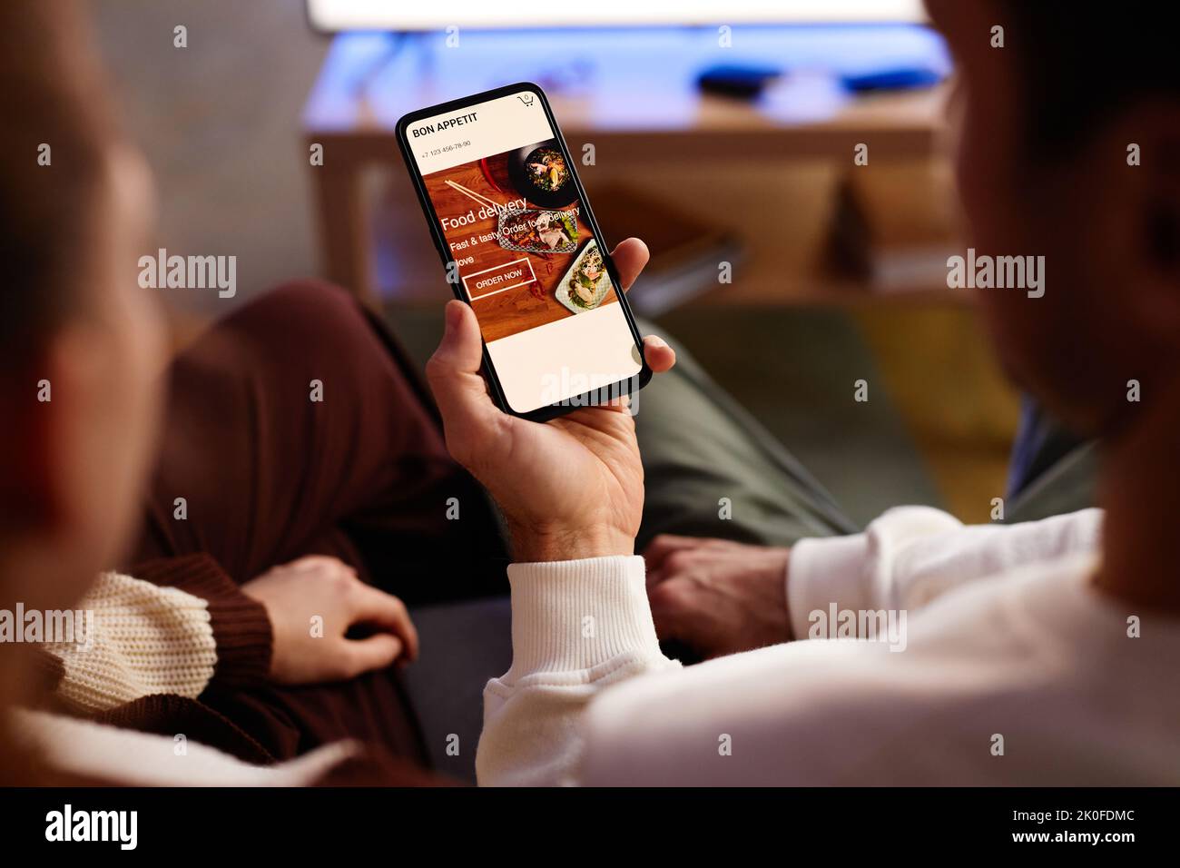 Primo piano di giovani coppie che ordinano cibo online sul telefono cellulare mentre si siedono a casa Foto Stock