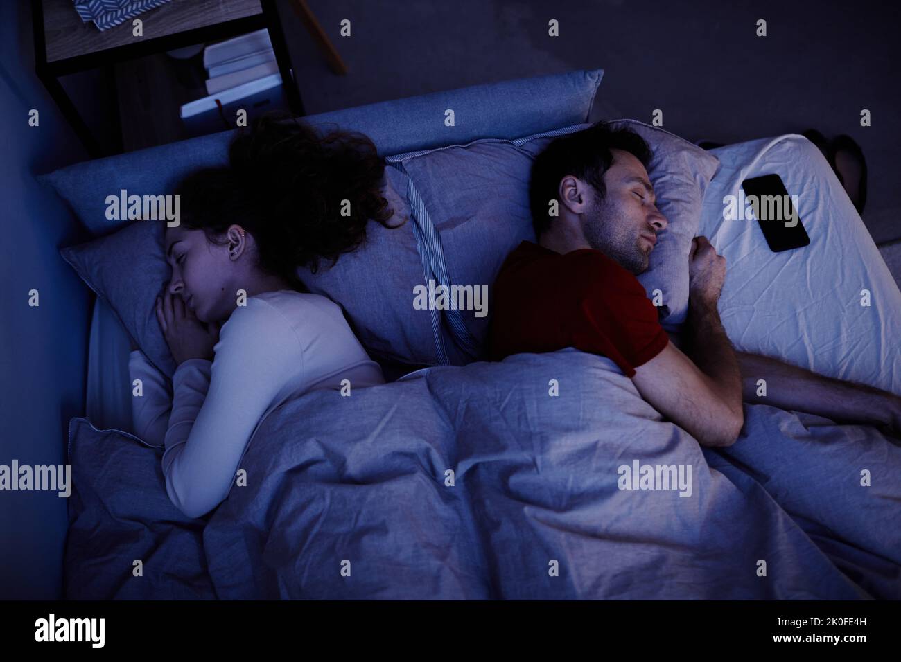 Vista ad alto angolo della giovane coppia che dorme sotto la coperta nel letto di notte Foto Stock