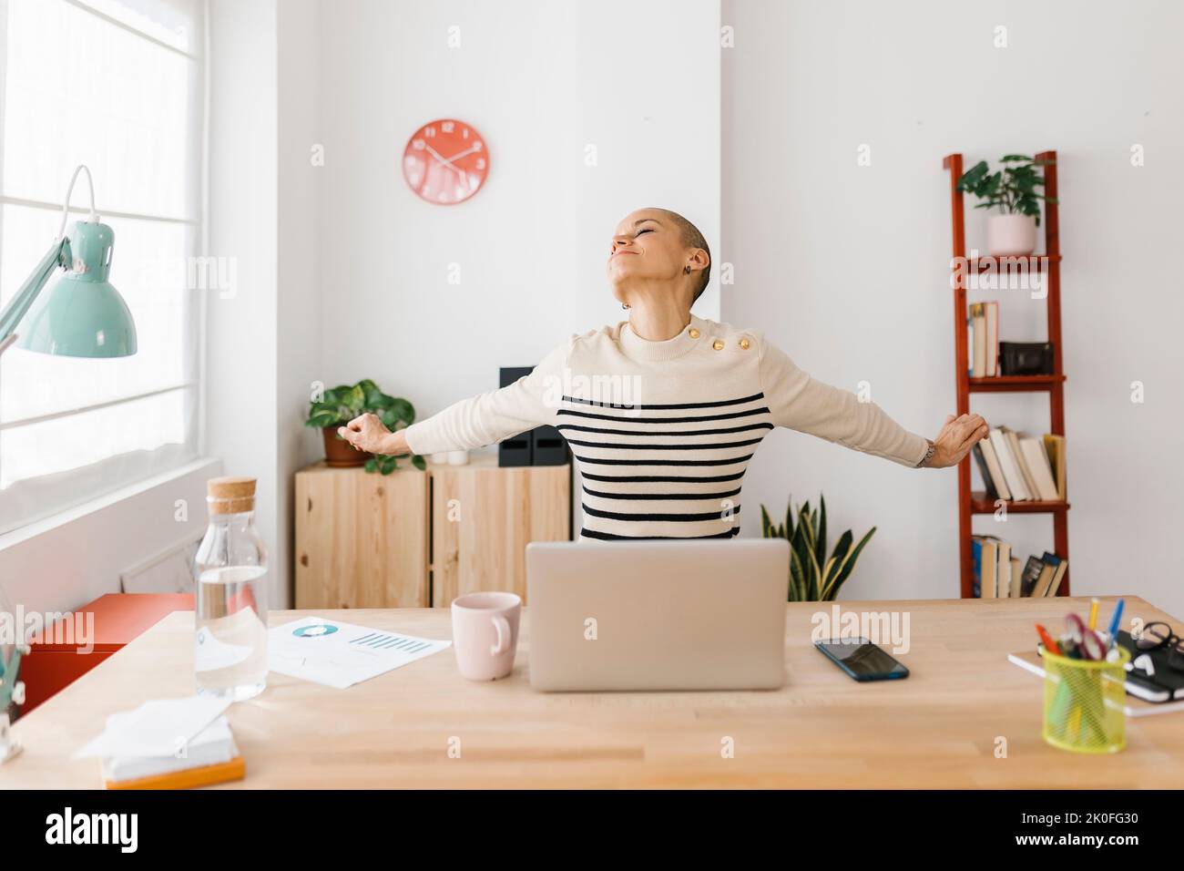 Donna adulta sorridente che stretching il corpo mentre lavora su un computer portatile in ufficio Foto Stock