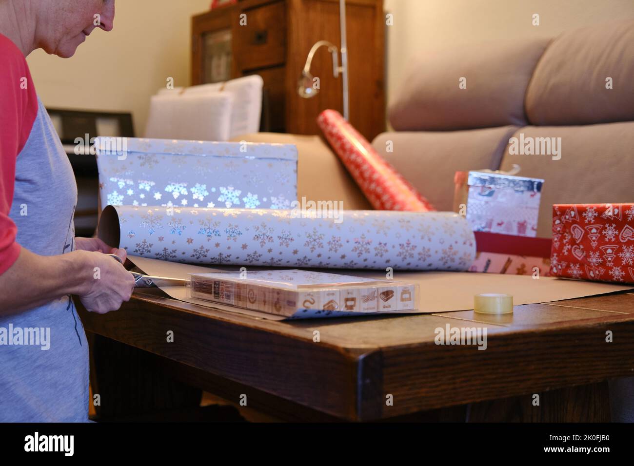 Una donna che taglia fuori la carta di Natale per avvolgere i regali. Foto Stock
