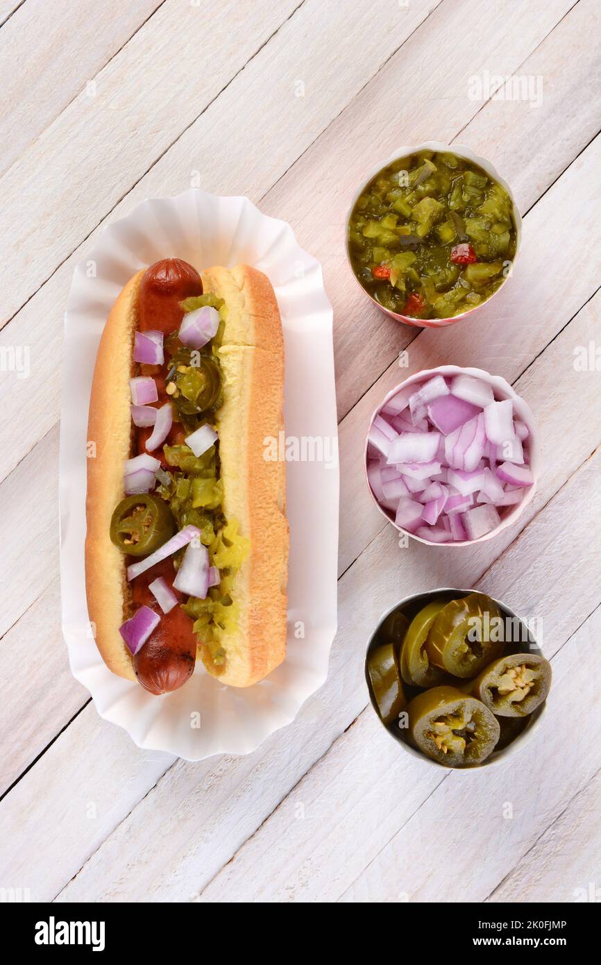 La vita ferma di un tavolo da picnic estivo con un hot dog soffocato in cipolle e jalapenos. Tre tazze di condimenti sono allineati accanto a. Foto Stock