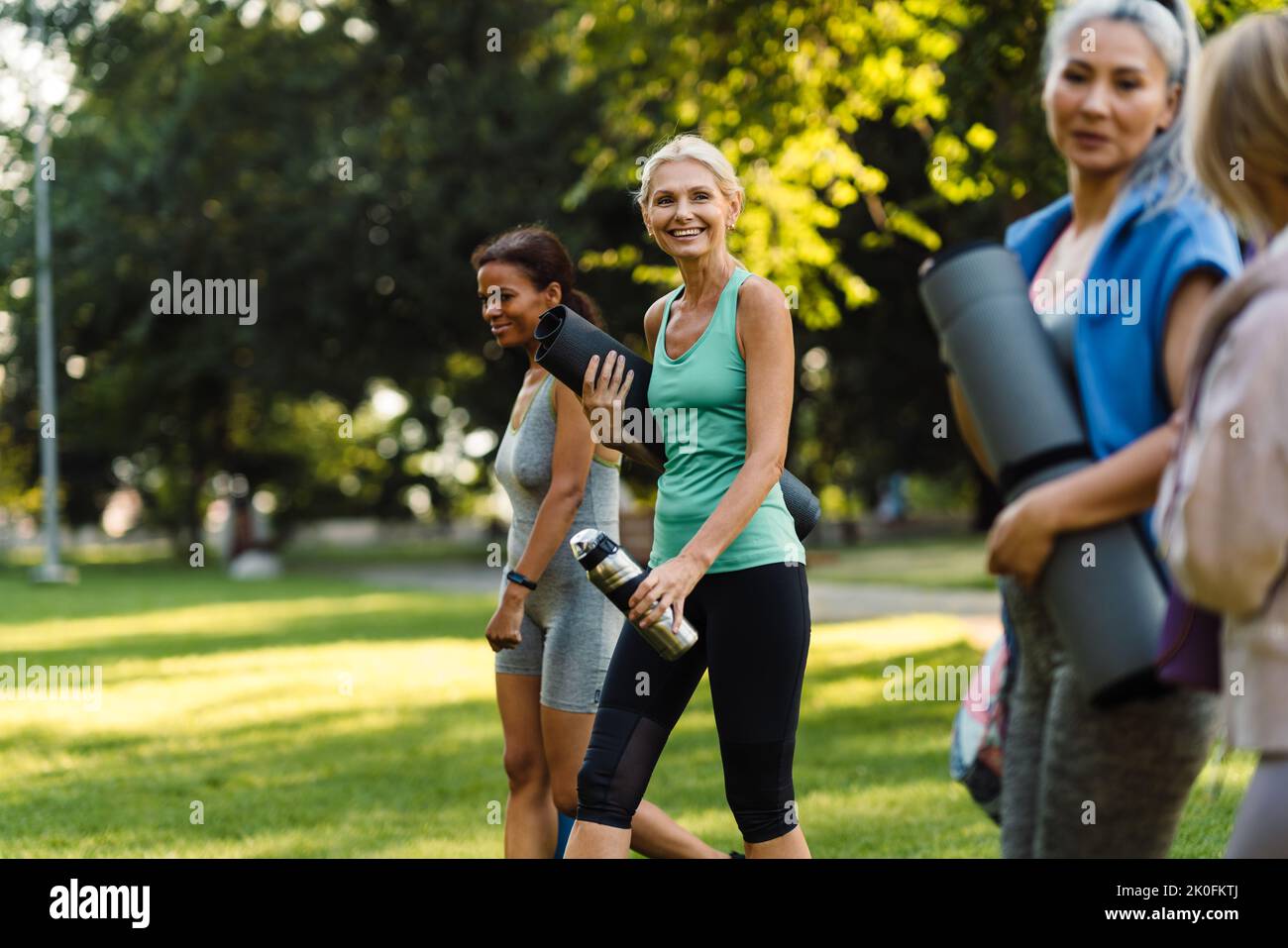 Donne multirazziali che parlano e sorridono dopo la pratica di yoga nel parco estivo Foto Stock