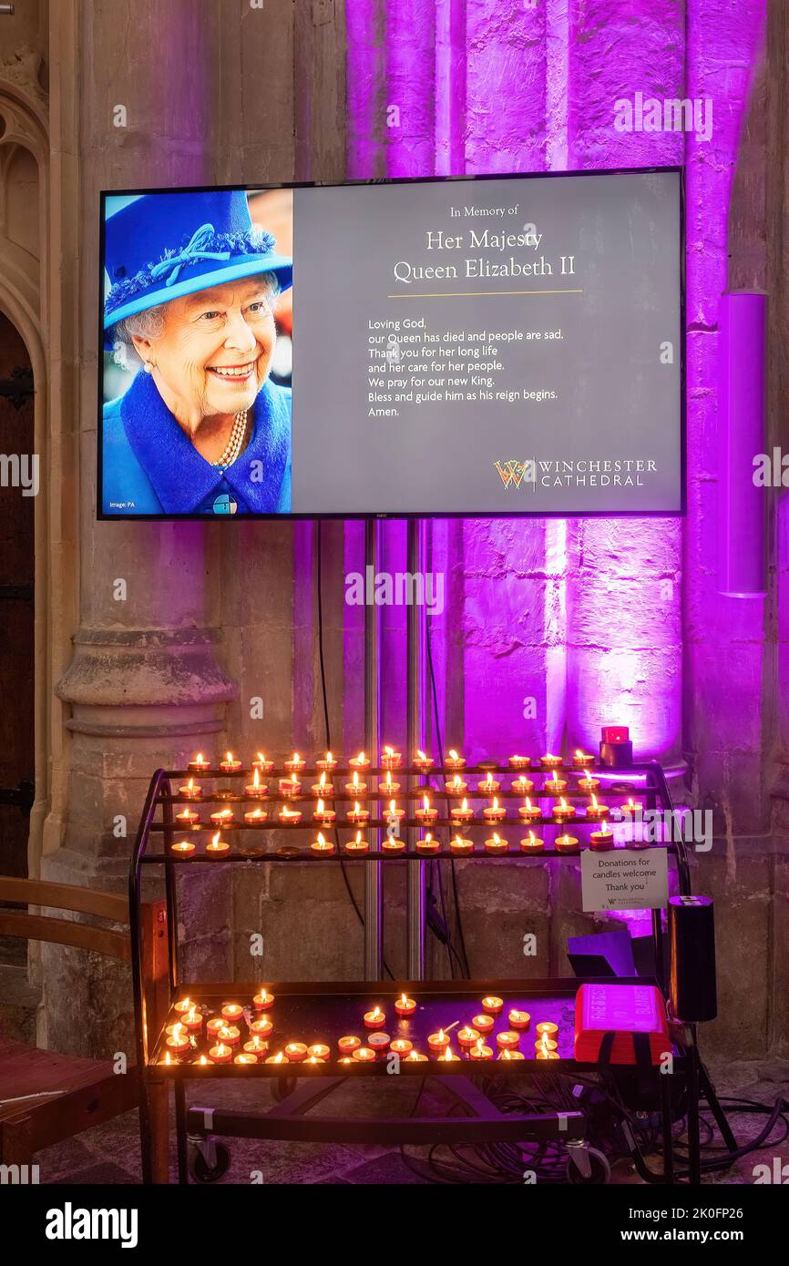 Winchester, Hampshire, Regno Unito. 11th settembre 2022. Dopo la morte della regina Elisabetta II, avvenuta il 8th settembre 2022, l'interno della cattedrale di Winchester è stato illuminato in viola, con immagini della regina, fiori e preghiere in mostra. Molte persone sono venute a pagare tranquillamente i loro rispetti oggi e a lasciare i loro tributi, firmando un libro di condoglianze o accendendo candele. Il paese è in un periodo di lutto nazionale fino al suo funerale. Foto Stock