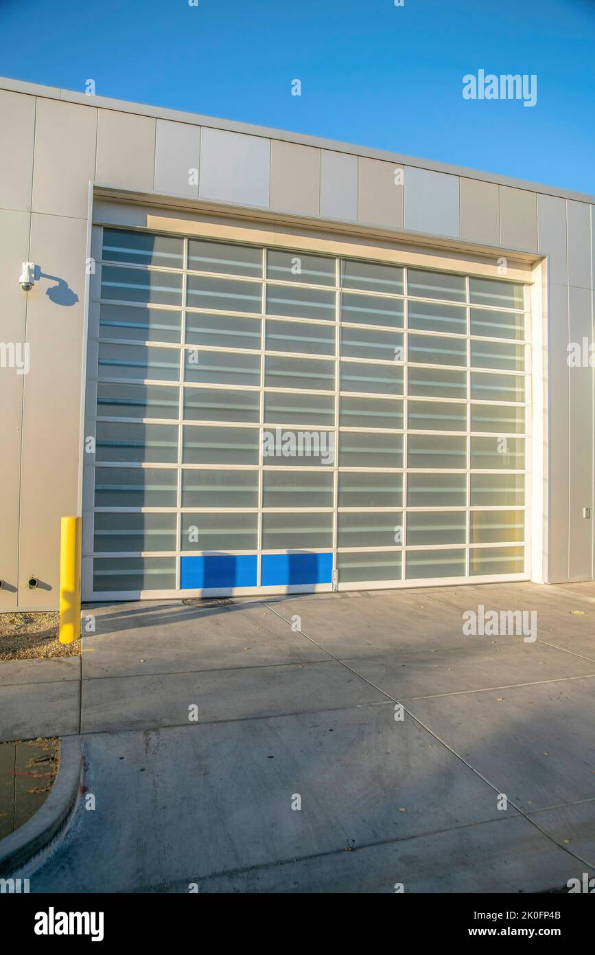 Garage esterno moderno con macchina fotografica di sicurezza e porta di vetro del garage-Phoenix, Arizona. Porta del garage a sezione alta con pannelli di vetro contro il cielo blu Foto Stock