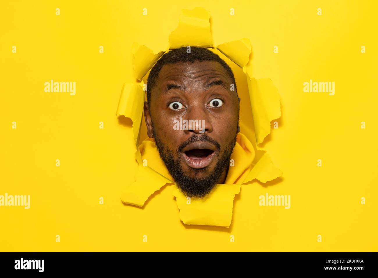 Scioccato afro-americano reagire con sorpresa, guardando la macchina fotografica, posando in lacerato giallo buco di carta Foto Stock