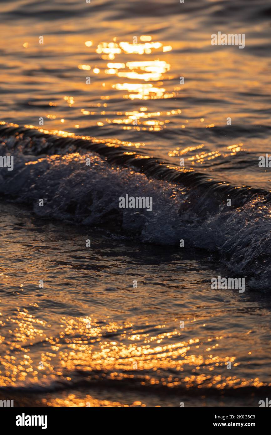 L'onda di mare spruzza da vicino. Ondulazione della superficie dell'acqua di mare con luce dorata del tramonto. Foto Stock
