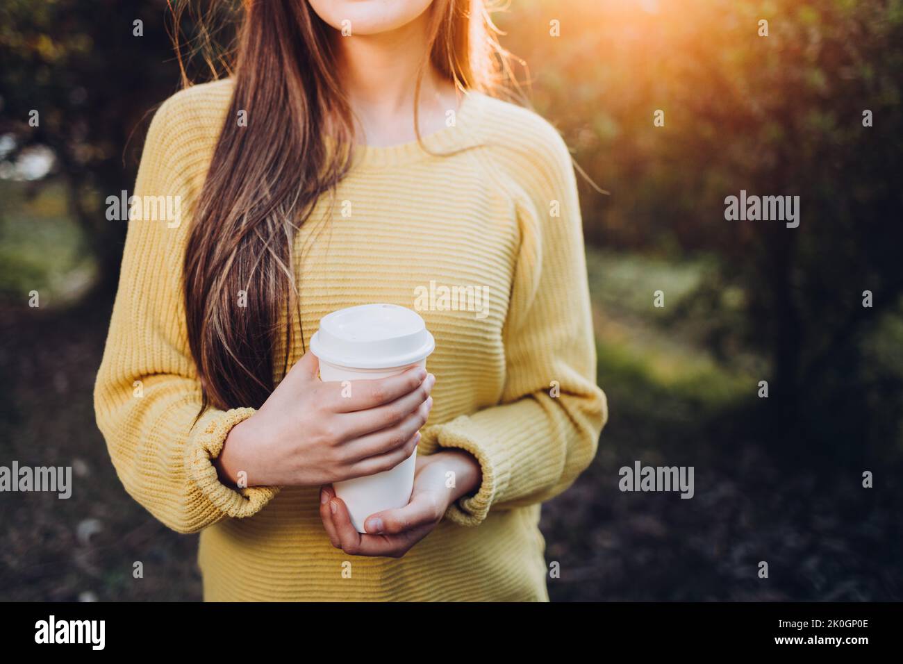 Ragazza giovane irriconoscibile che indossa un maglione giallo e tiene una tazza di caffè bianco nel parco. Atmosfera autunnale Foto Stock