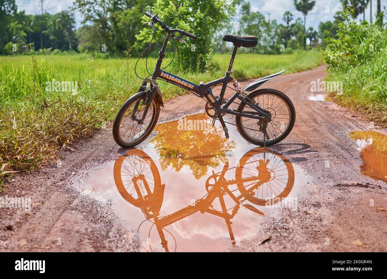 Una bicicletta di montagna e riflessione in una pozza d'acqua su una strada di campagna. Foto Stock