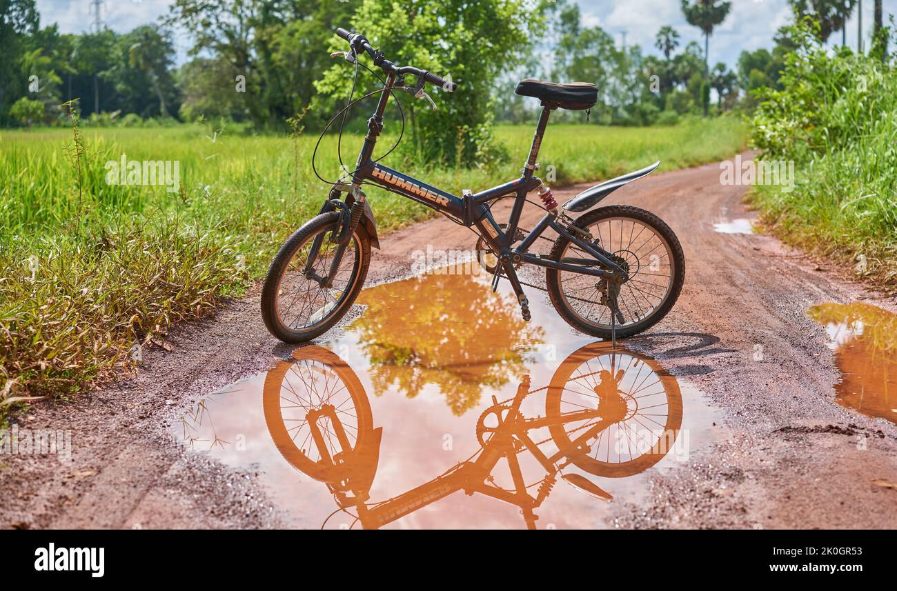 Una bicicletta di montagna e riflessione in una pozza d'acqua su una strada di campagna. Foto Stock