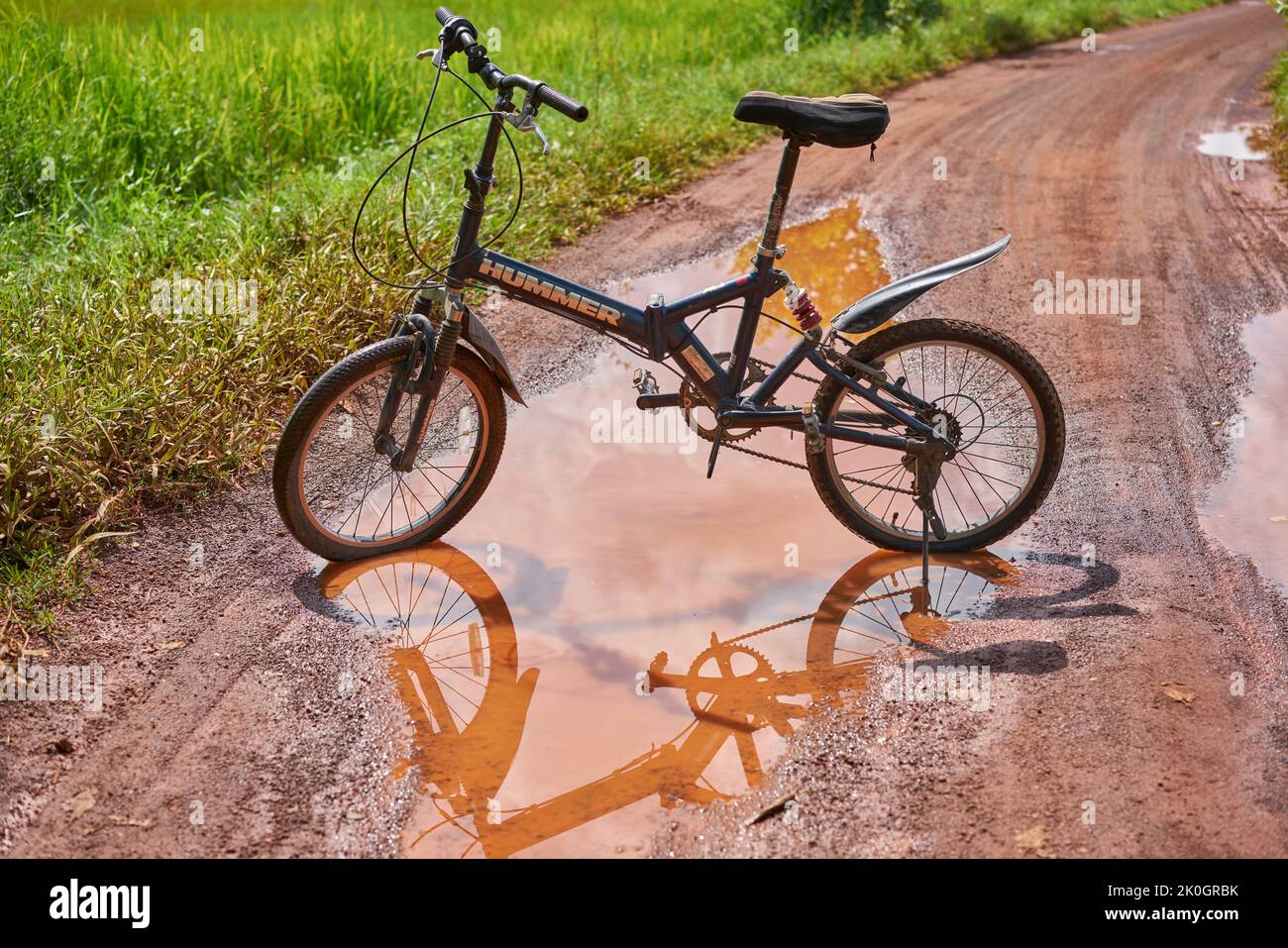 Una bicicletta di montagna e riflessione in una pozza d'acqua su una strada di campagna. Foto Stock