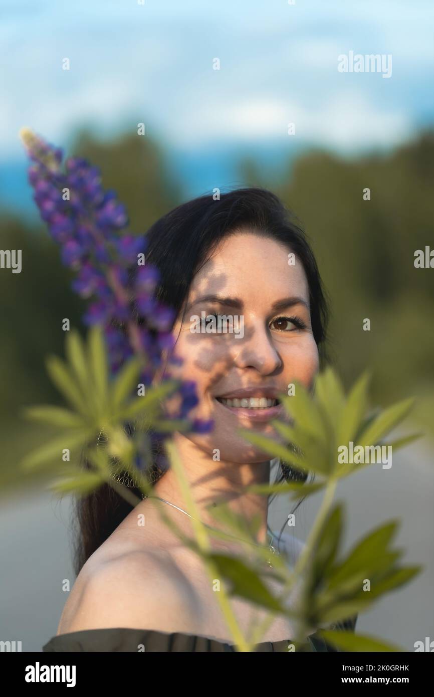 Una donna attraente in un campo con un bouquet estivo di fiori selvatici Lupinus. Foto verticale. Foto Stock